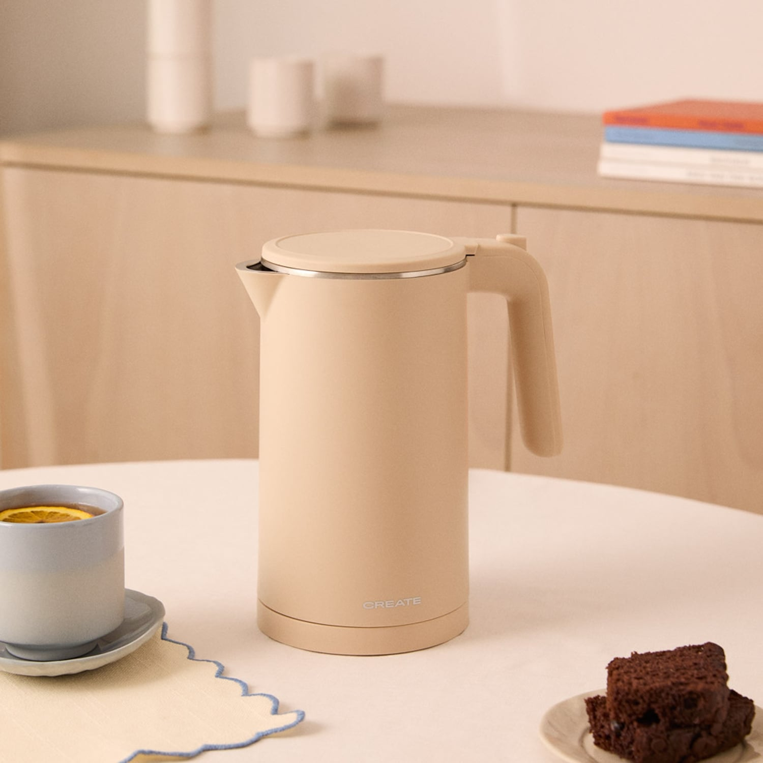 Una tetera beige sobre una mesa con una taza de té y pastel.