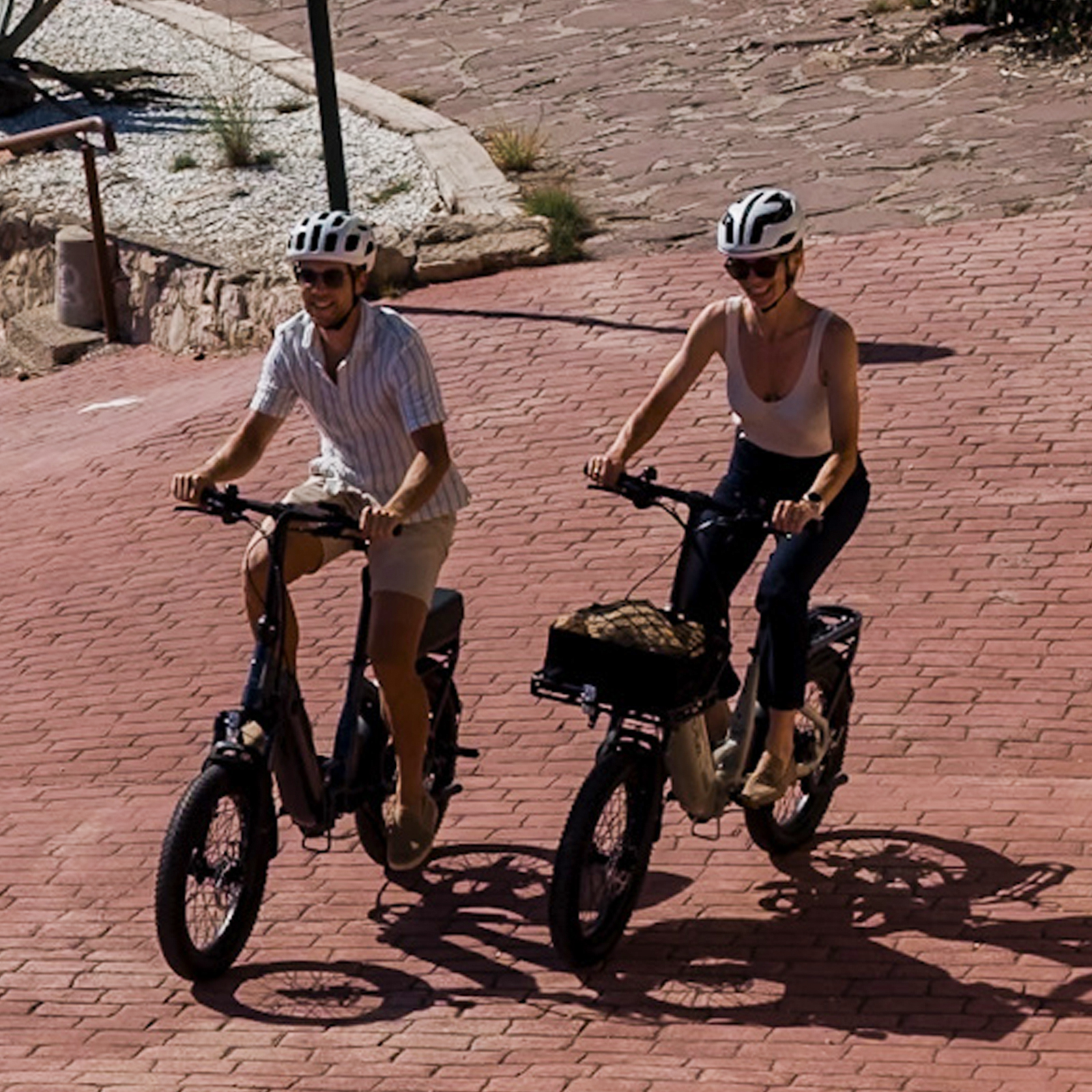 Zwei Personen fahren E-Bikes auf einer roten Ziegelsteinpromenade.