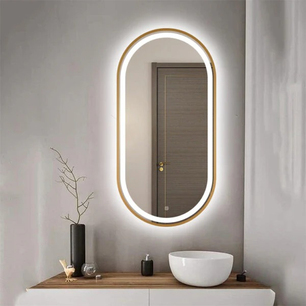 An oval mirror with a gold frame and integrated lighting hangs above a vanity counter.