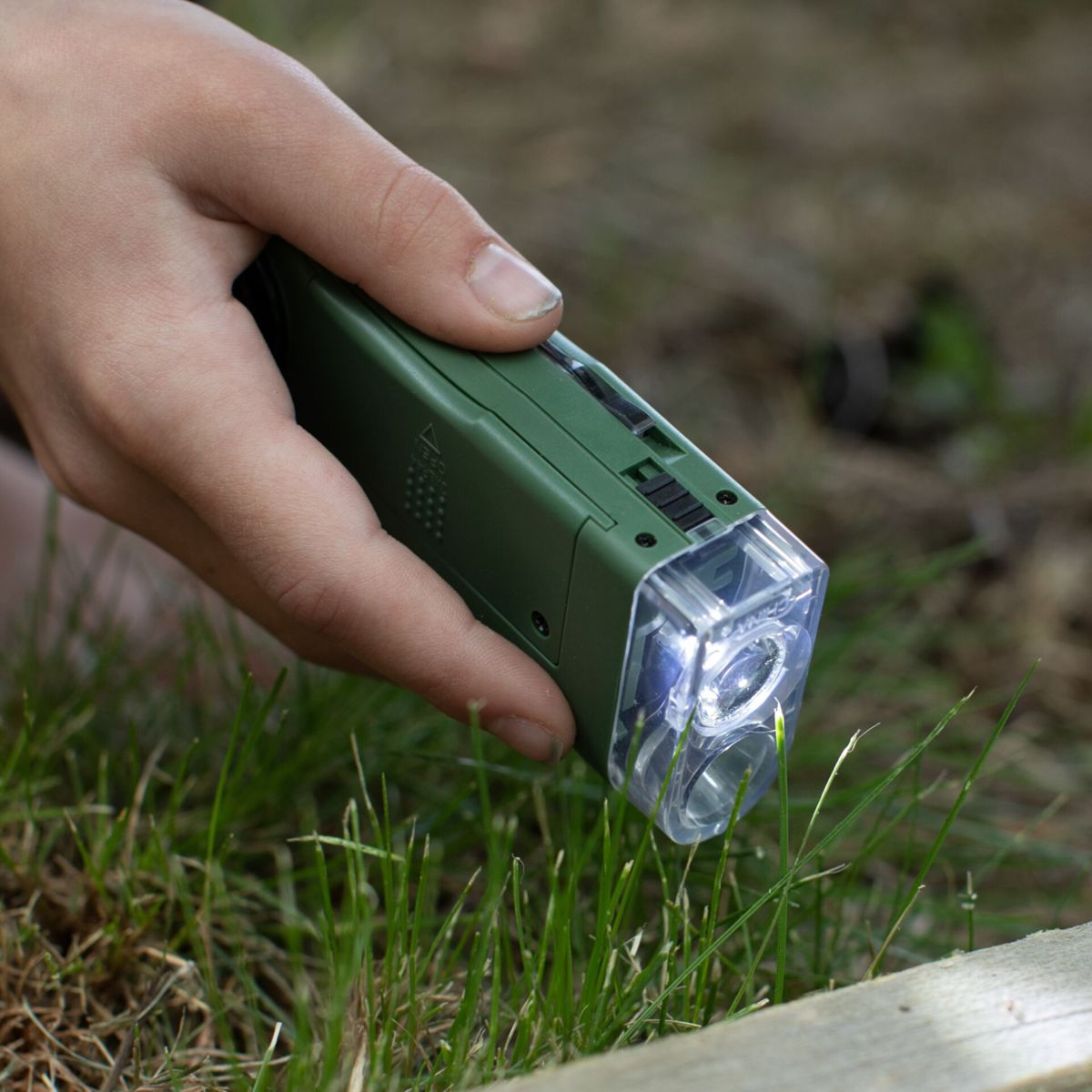 Eine Hand hält eine grüne Taschenlampe über Gras.