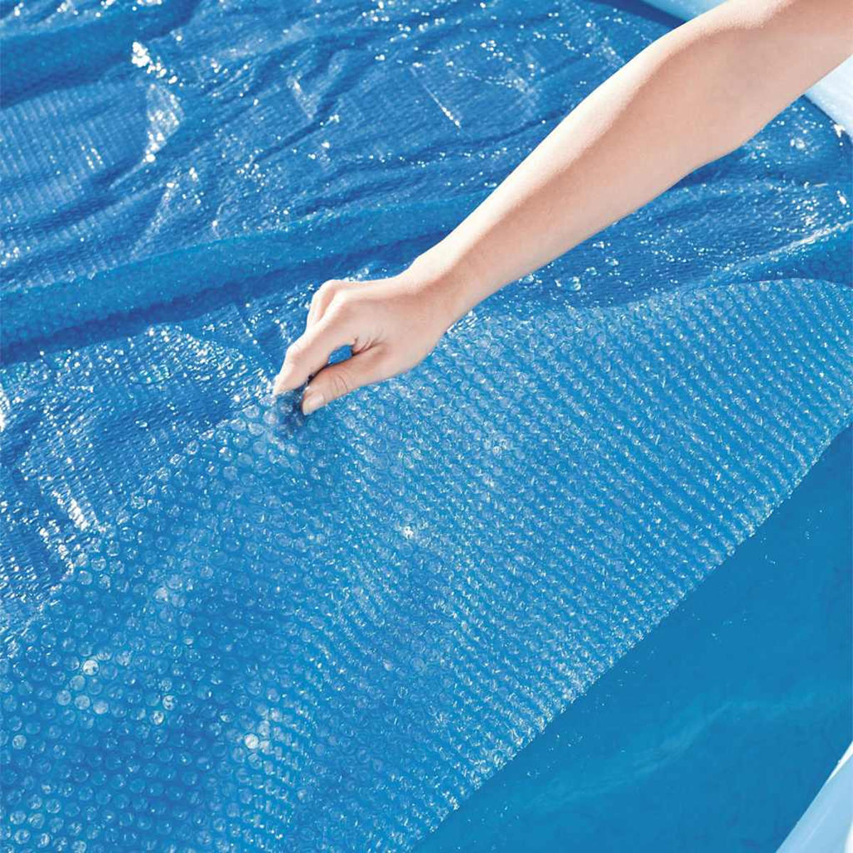 Una mano levanta una cubierta de burbujas azul de una piscina.