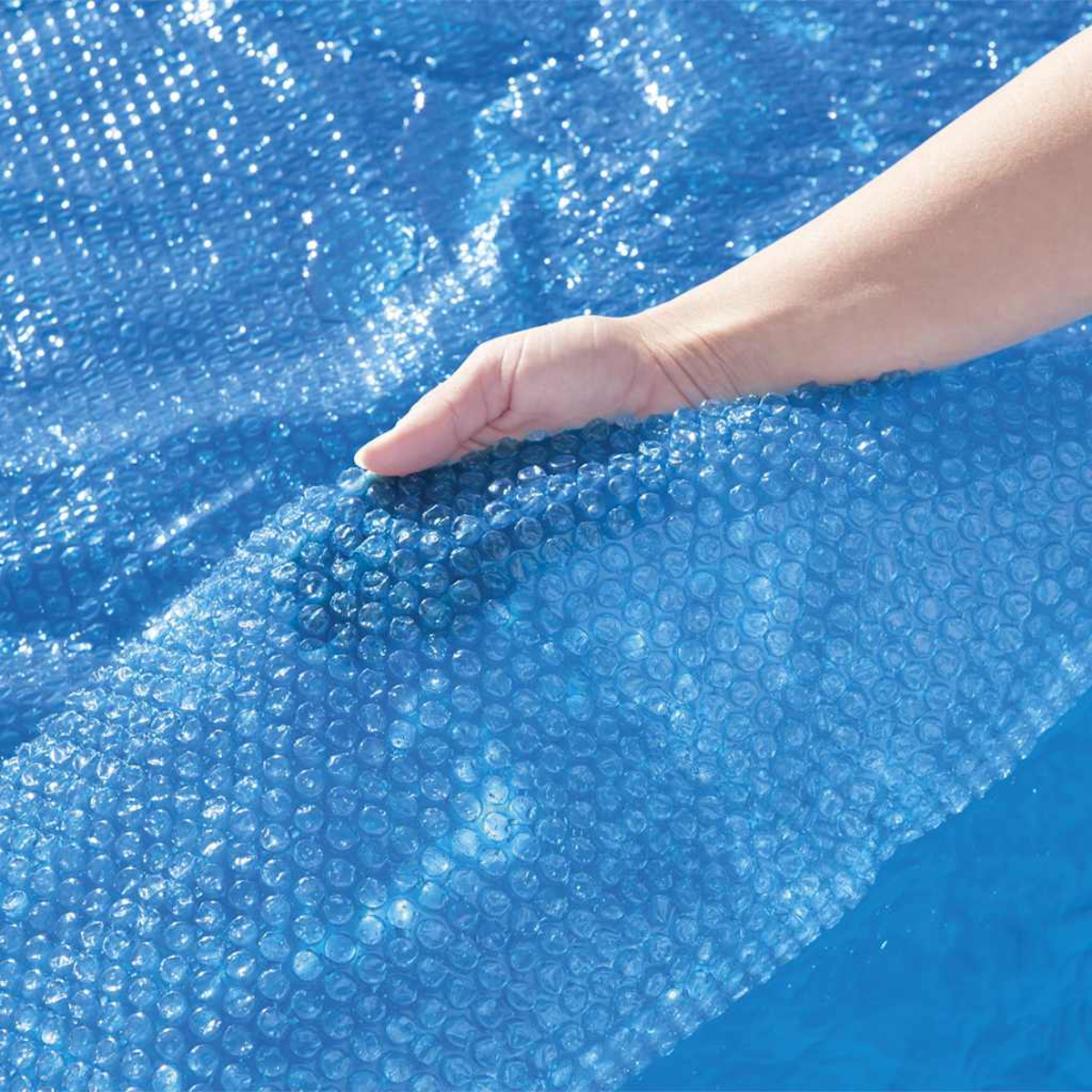 Una mano levanta una cubierta de burbujas azul de una piscina.