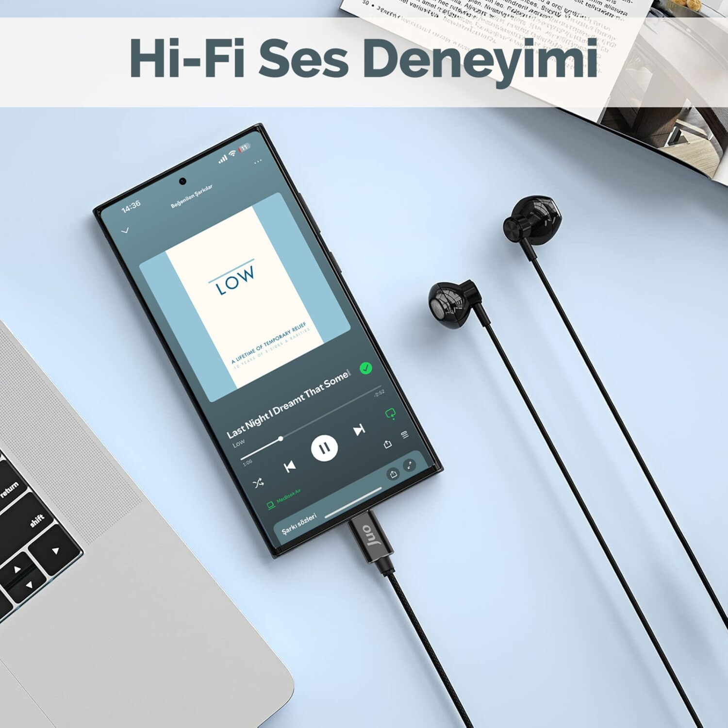 Müzik çalan bir akıllı telefona bağlı siyah kulaklıklar. Yanında bir dizüstü bilgisayar.