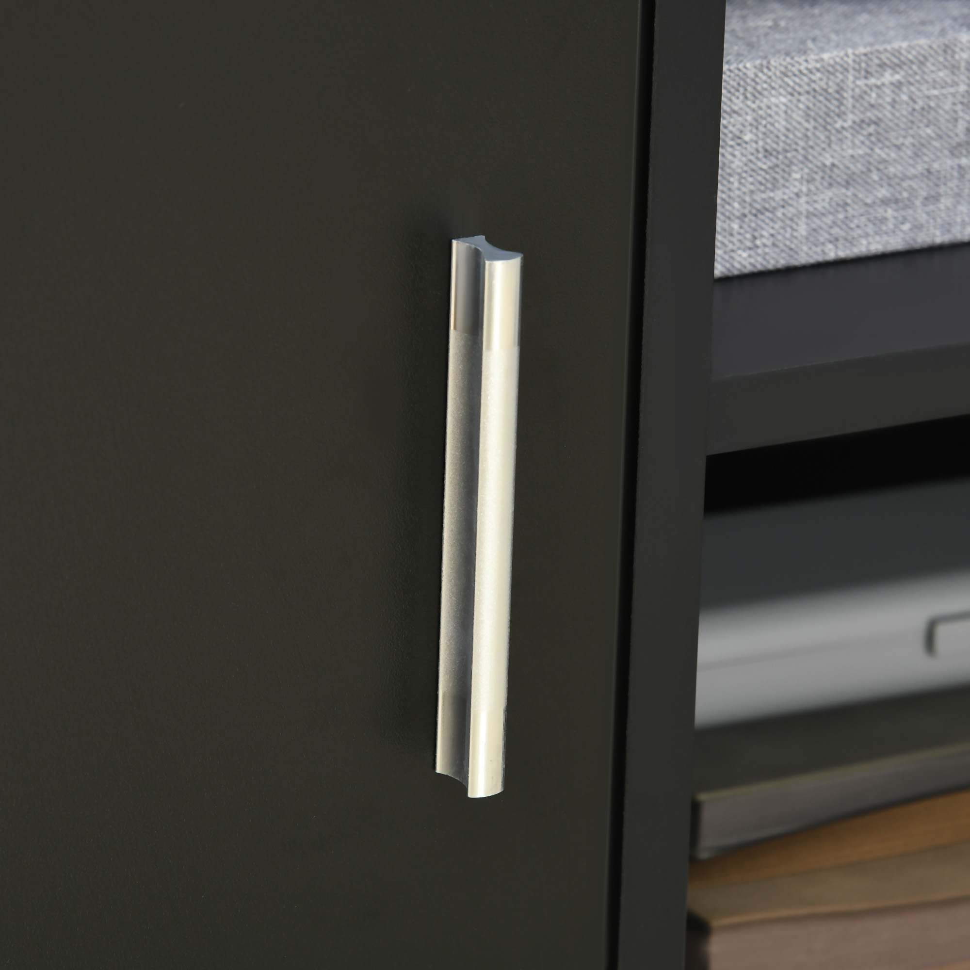 Puerta de armario negra con tirador plateado. Estante con textil gris y libros.