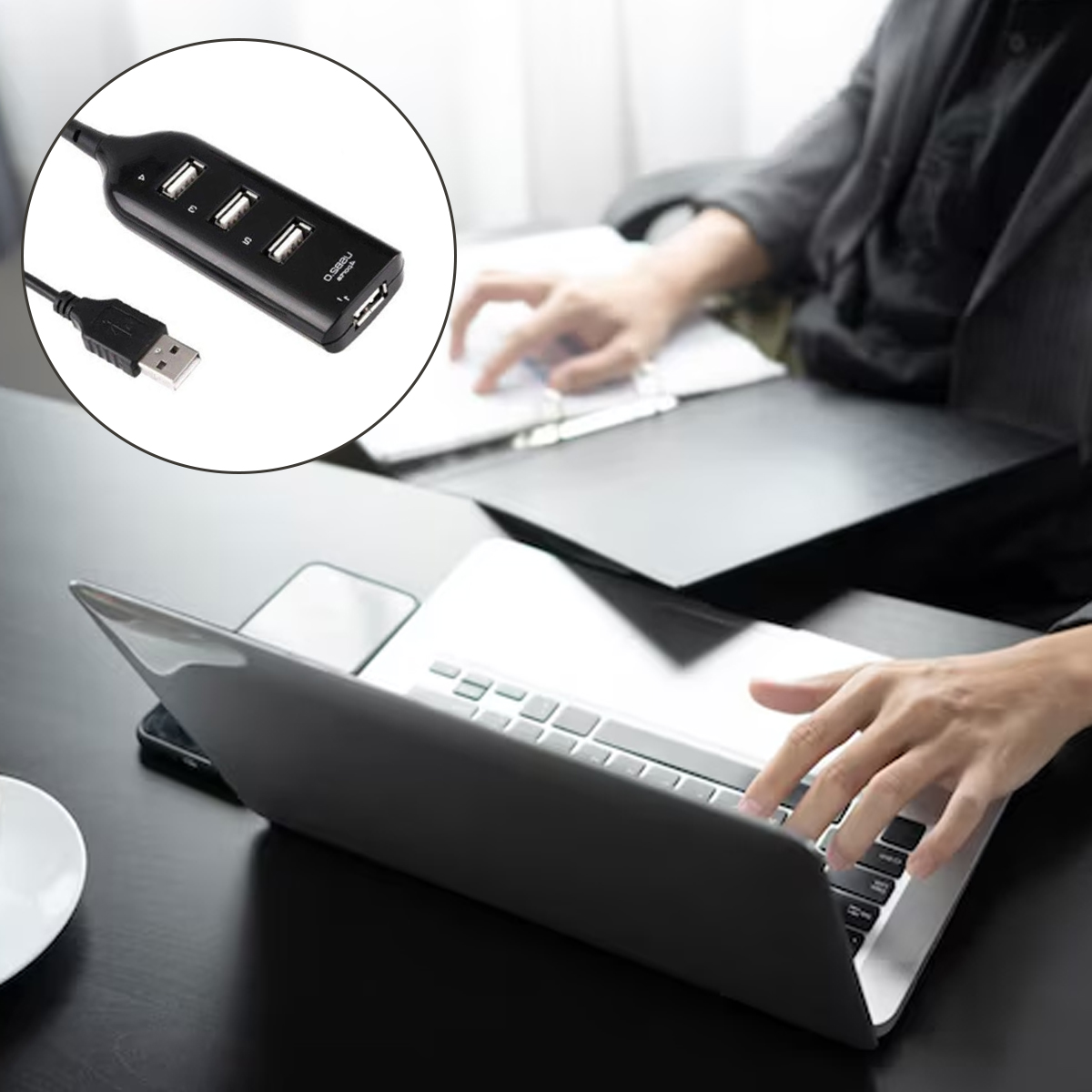 Ein schwarzer USB-Hub mit vier Anschlüssen ist neben einem Laptop abgebildet. Eine Person tippt auf dem Laptop.