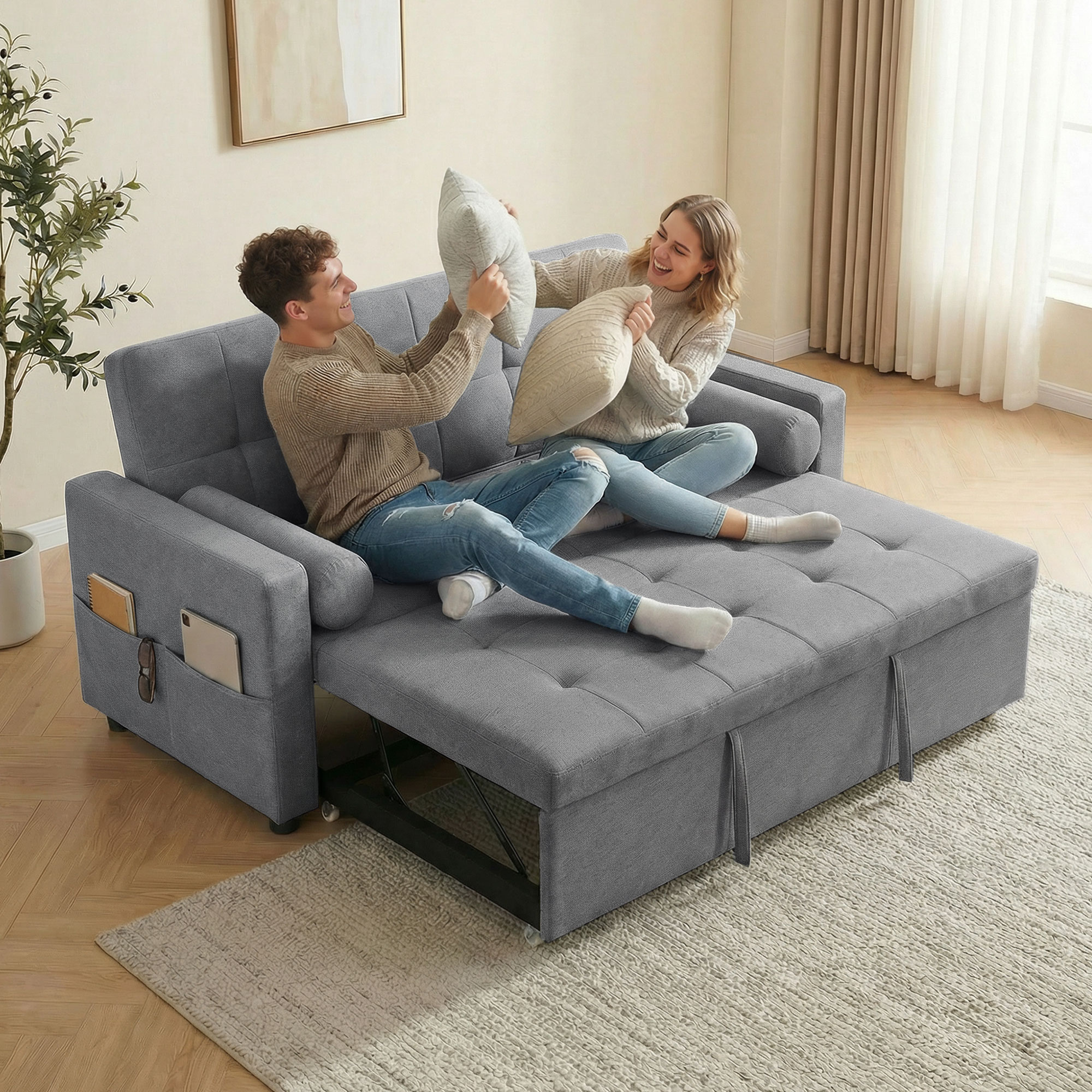 Una pareja lanza cojines en un sofá cama gris en una habitación luminosa.