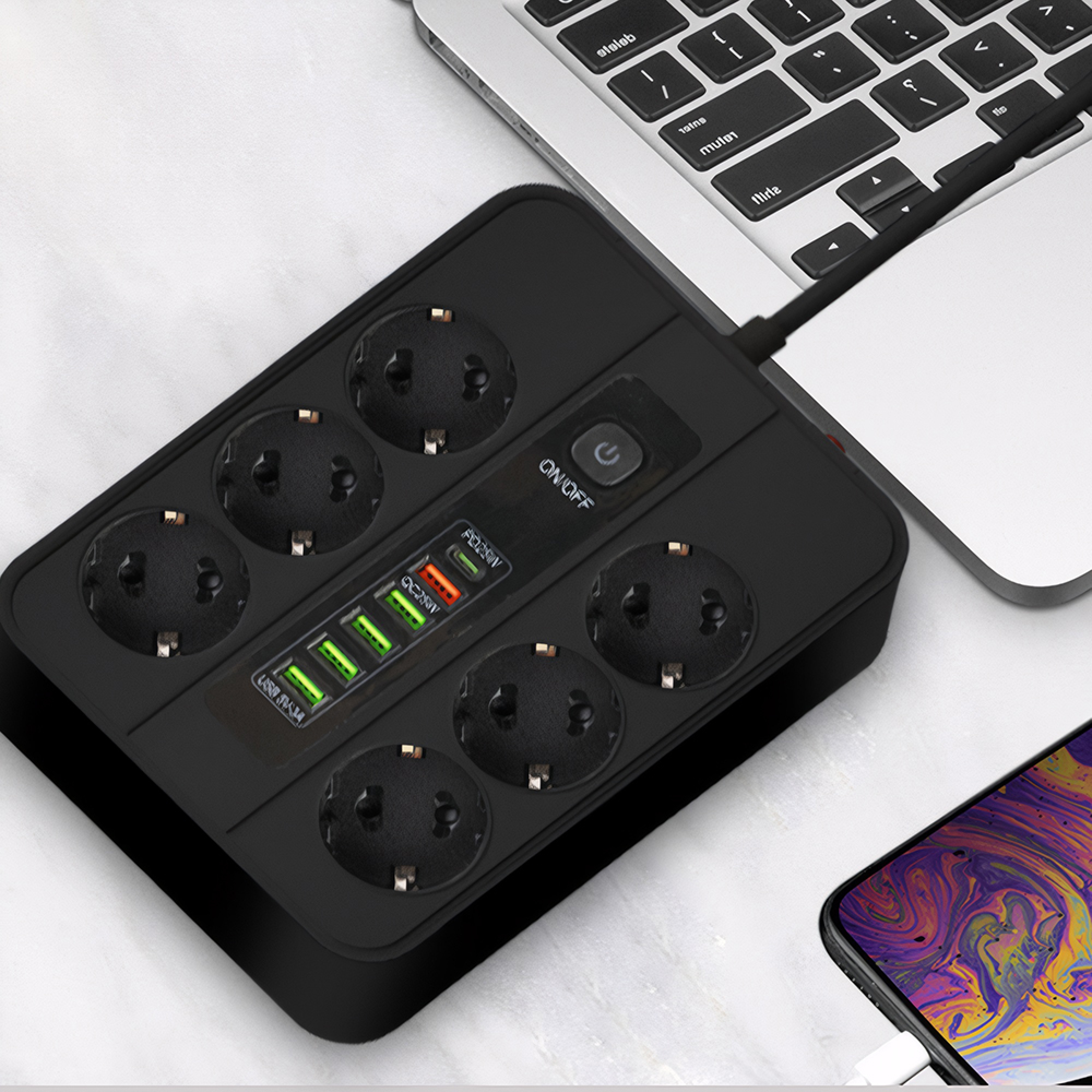 Schwarzer Mehrfachstecker mit USB-Ports neben einem Laptop und Handy.