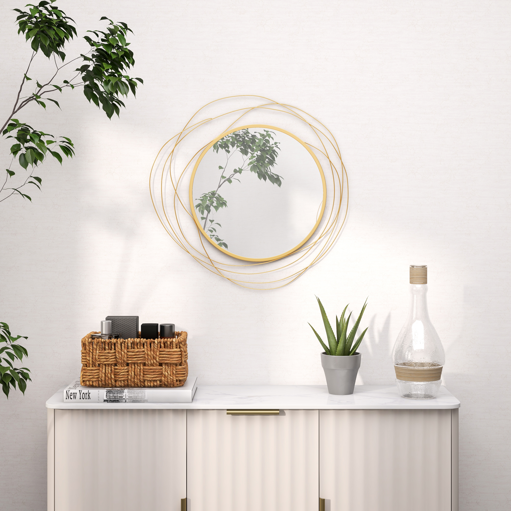 Un espejo redondo con marco dorado cuelga sobre una cómoda con plantas y decoración.