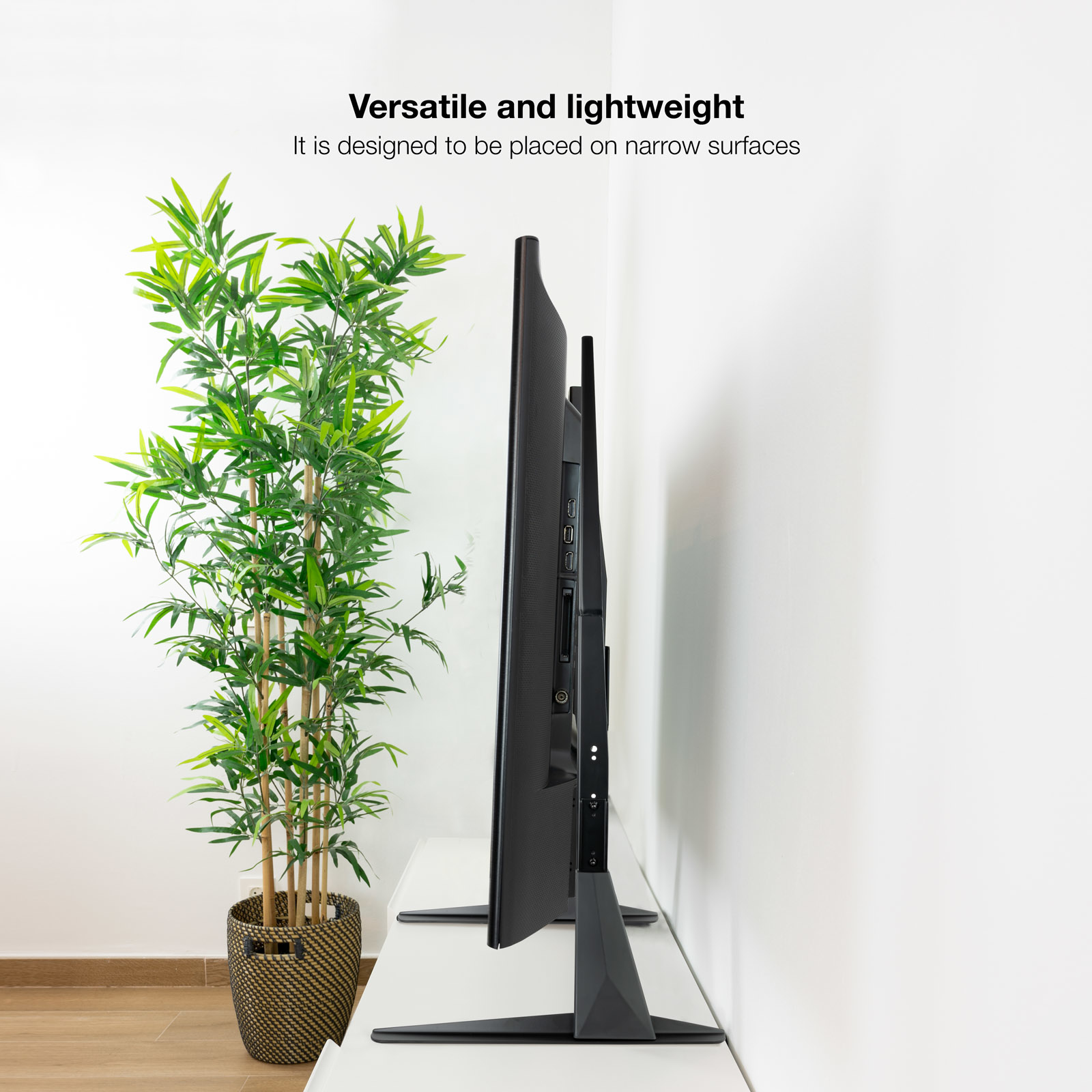 Un televisor negro se sienta junto a una planta en maceta con hojas de bambú.