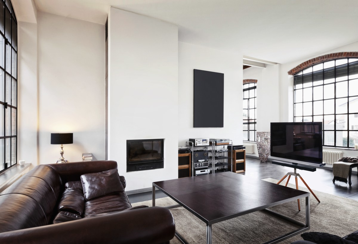 Ein großes Wohnzimmer mit Ledersofa, Kamin, Fernseher und Fenstern.