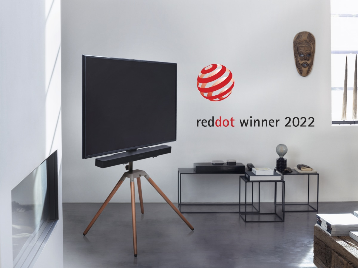 Ein Fernseher auf einem Stativ mit Holzbeinen steht neben einem Kamin.