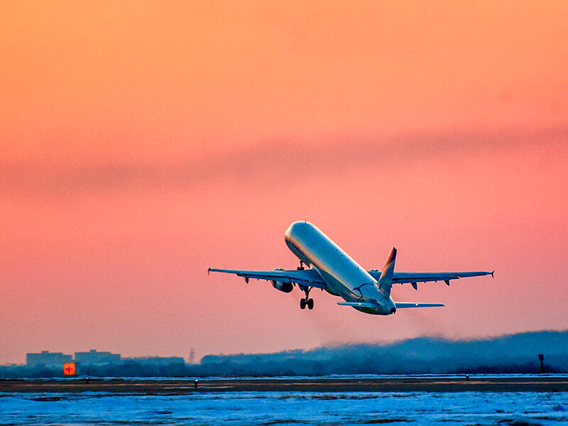 Un avión despegando en el atardecer desde un aeropuerto, con el cielo anaranjado.