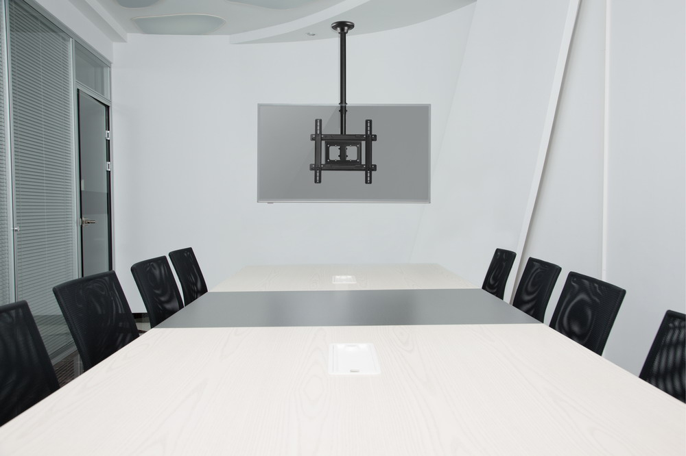 Een vergaderruimte met een lange tafel, zwarte stoelen en een plafondbeugel voor een scherm.