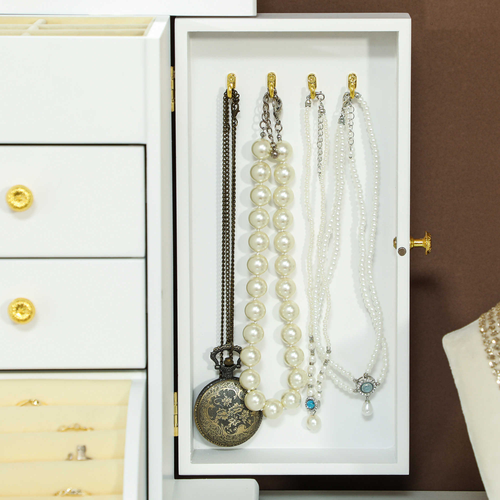 Una caja de joyería blanca está abierta, mostrando collares y un reloj de bolsillo.