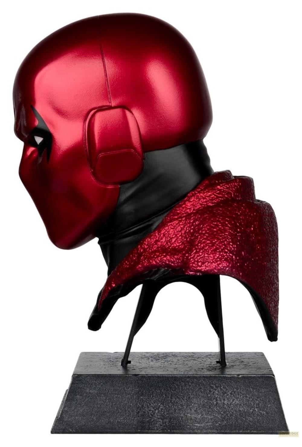 Rote Maske mit schwarzem Kragen, auf einem schwarzen Sockel montiert.