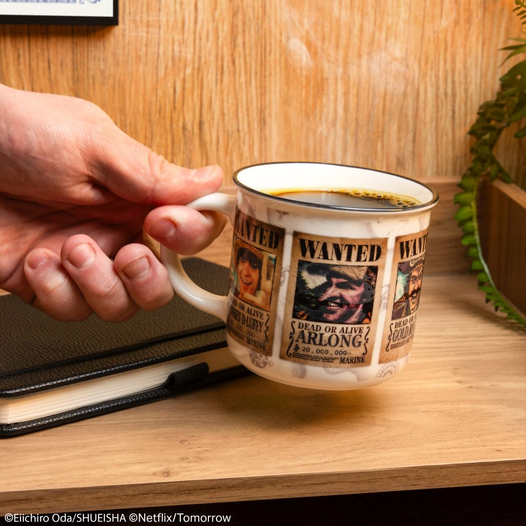 Eine Hand hält eine Kaffeetasse mit Anime-Steckbriefen. Auf dem Tisch liegt ein Notizbuch.