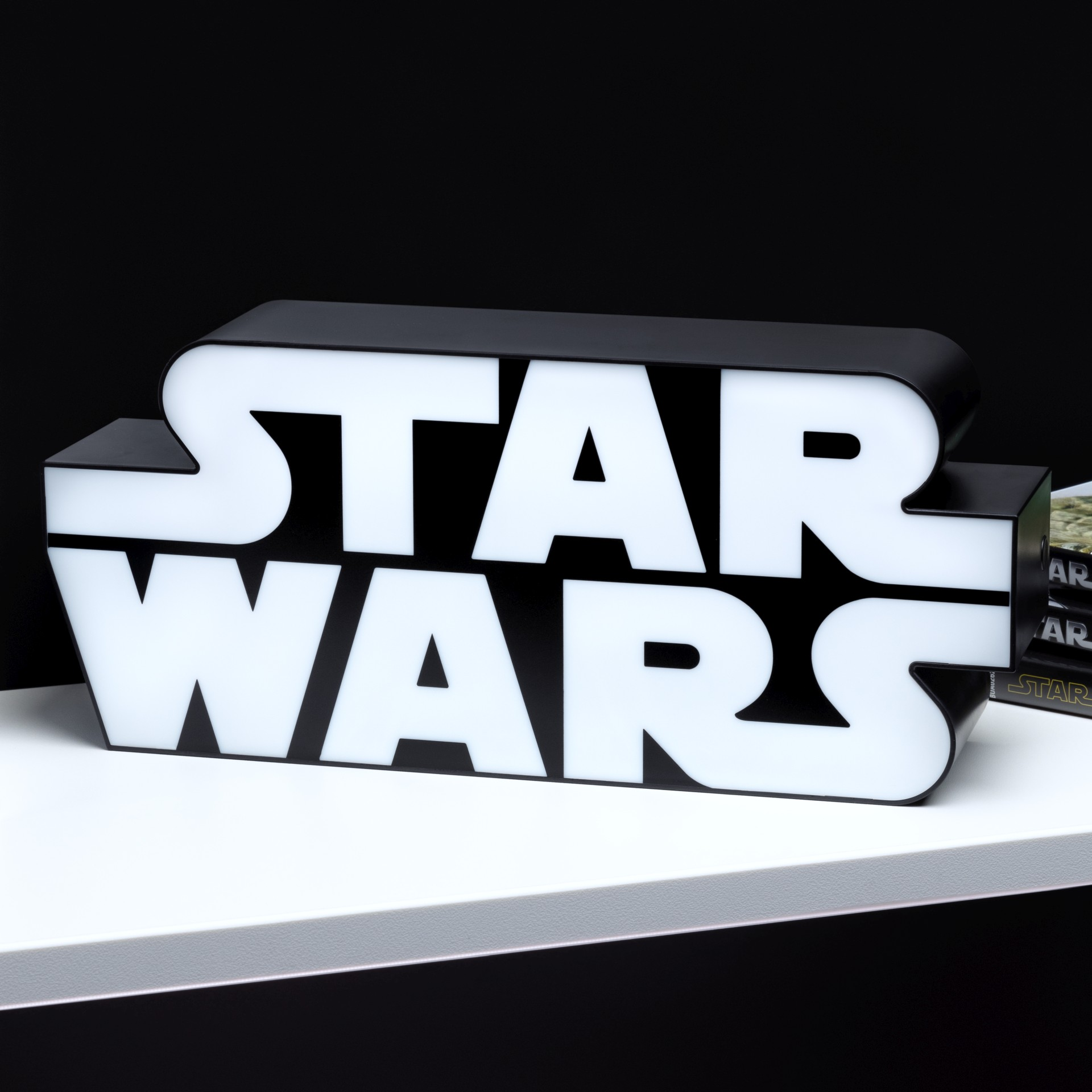 Ein beleuchtetes Star Wars Logo auf einem Regal vor schwarzem Hintergrund.