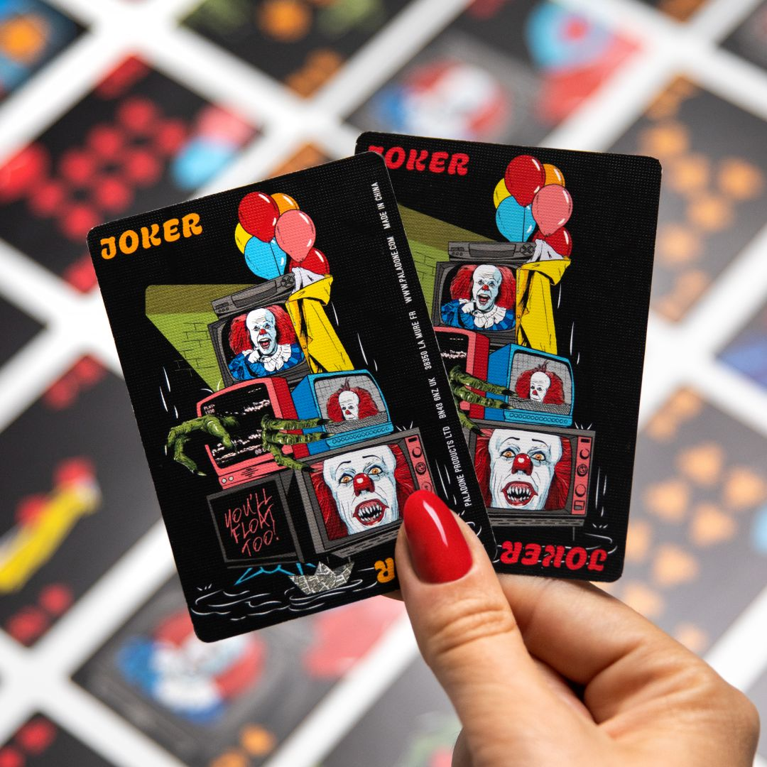 Una mano tiene due carte da gioco Joker con clown inquietanti e palloncini su TV.