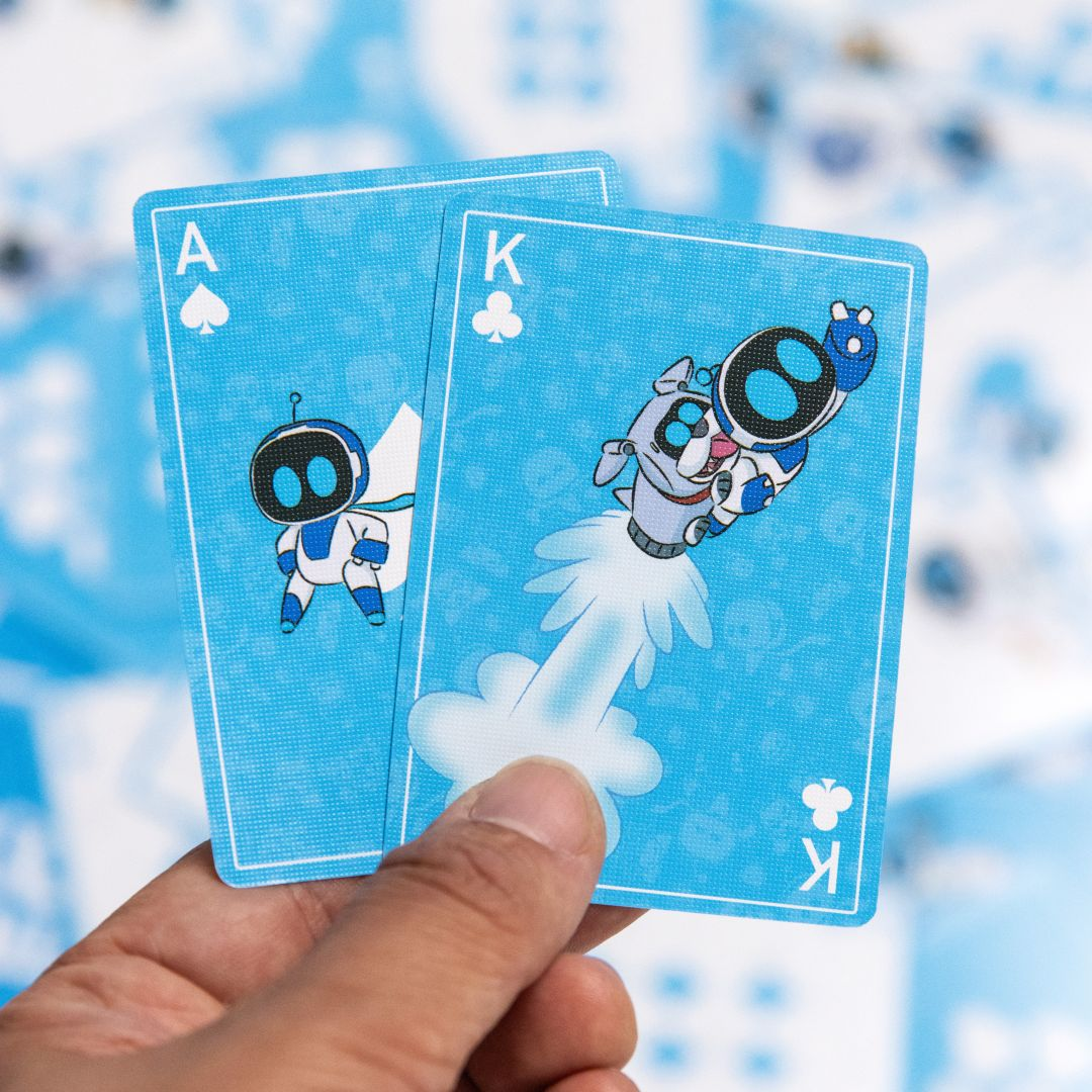 Une main tient un As et un Roi de cartes à jouer avec des robots dessinés. Fond bleu.