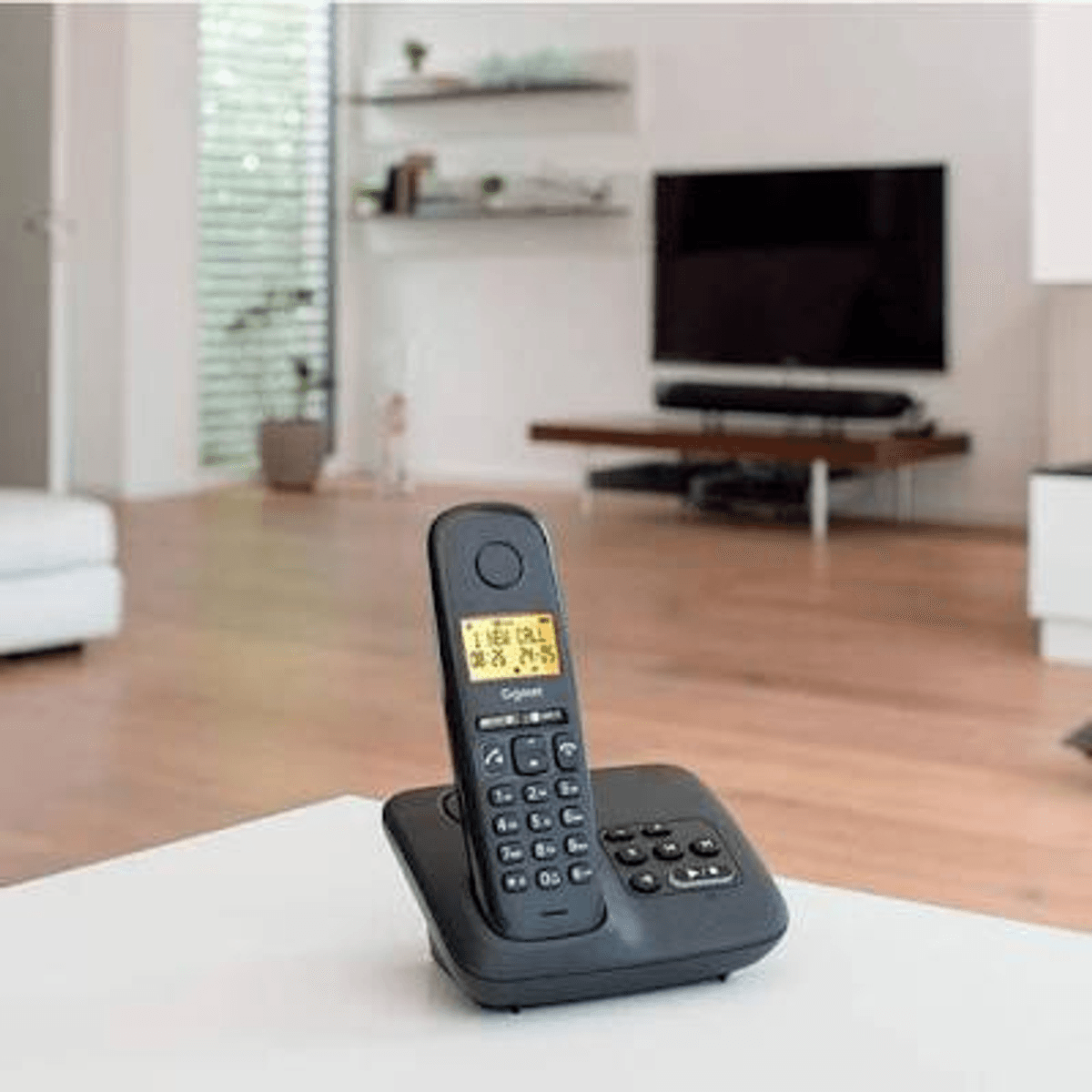 Un teléfono inalámbrico negro está sobre una mesa blanca en una sala de estar.