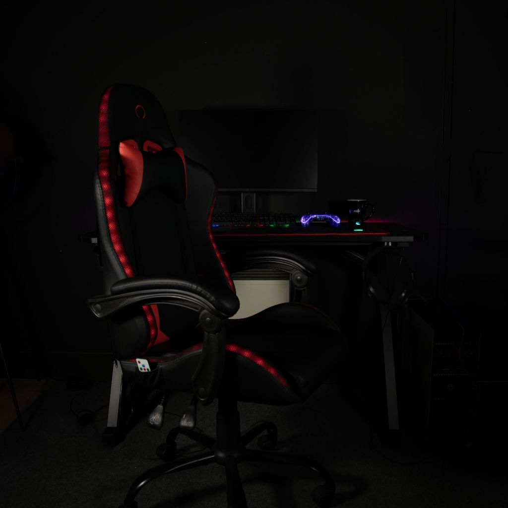 Ein schwarzer Gaming-Stuhl mit roten Akzenten steht vor einem Schreibtisch mit Computer.