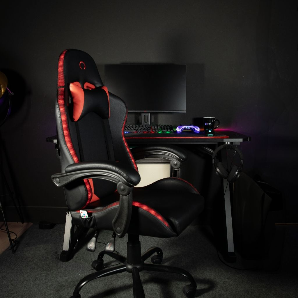 Schwarzer und roter Gaming-Stuhl vor einem Schreibtisch mit Monitor und Tastatur.