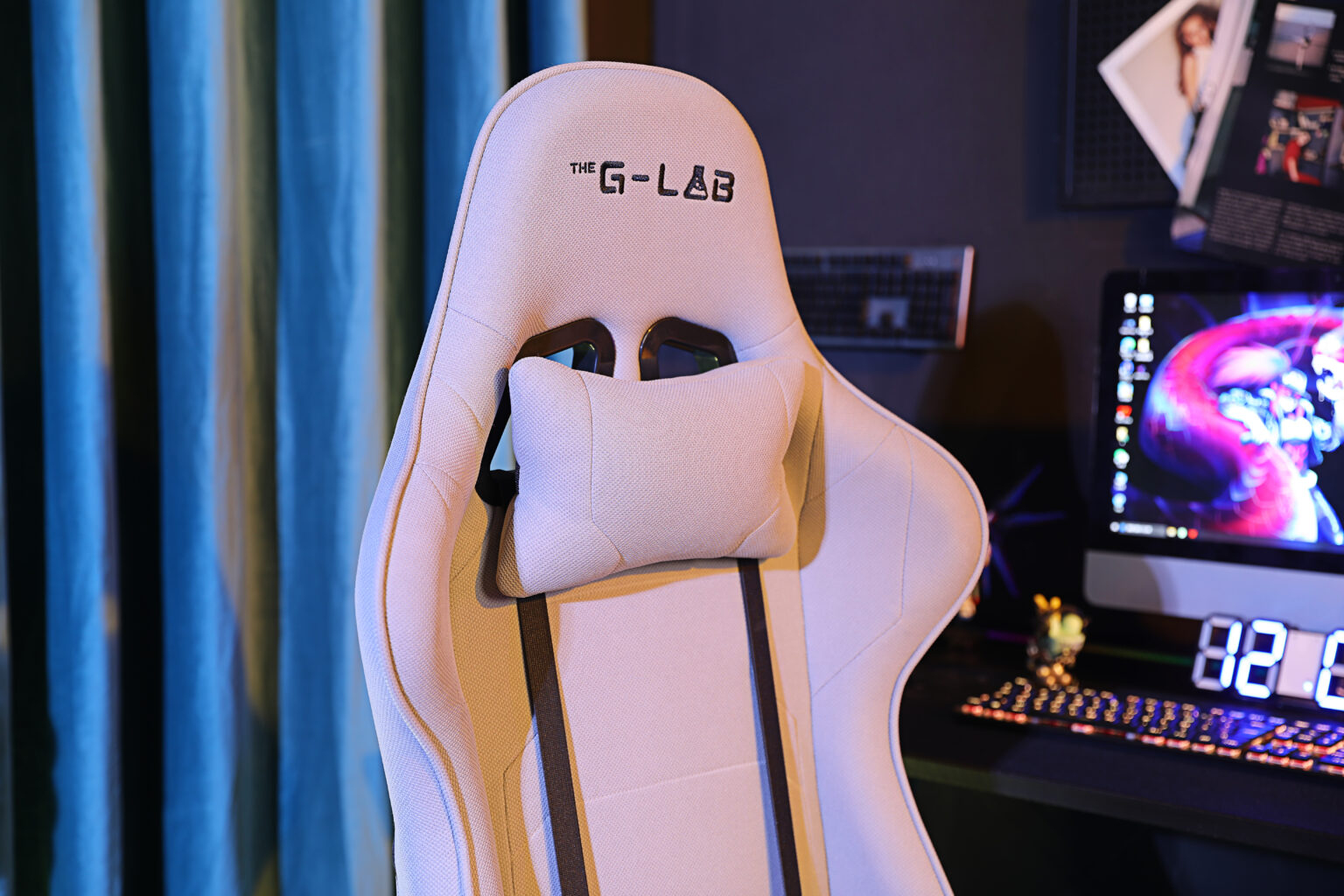 Una silla gamer blanca con cojín cervical, delante de un escritorio con teclado y pantalla.