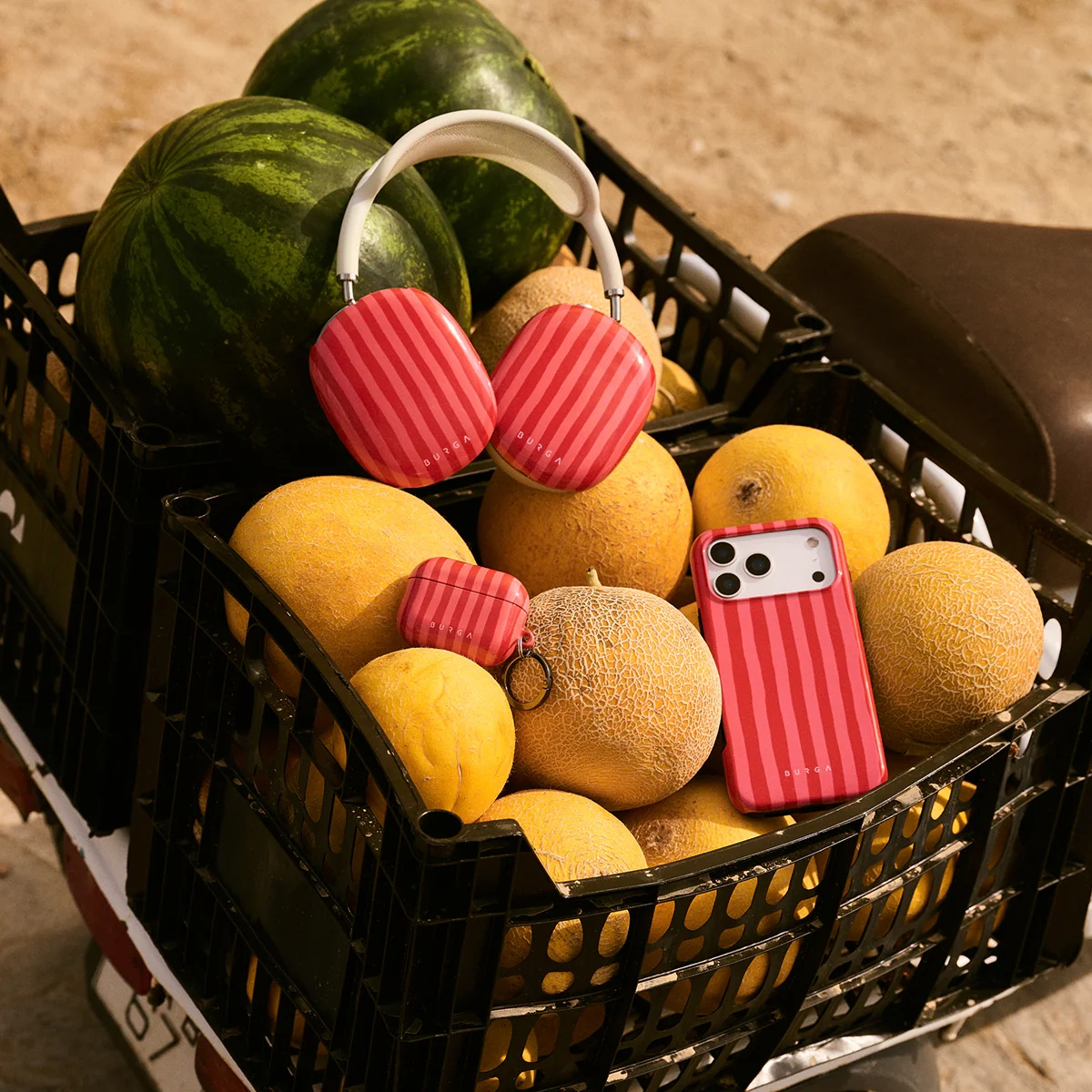 A black crate filled with melons and watermelons, featuring pink accessories.