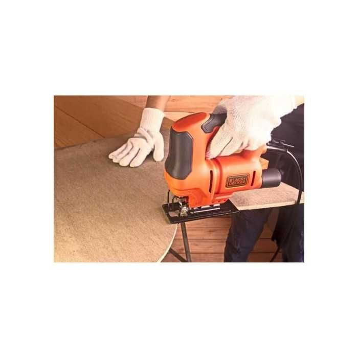 Persona con guanti bianchi usa seghetto alternativo arancione per tagliare legno.