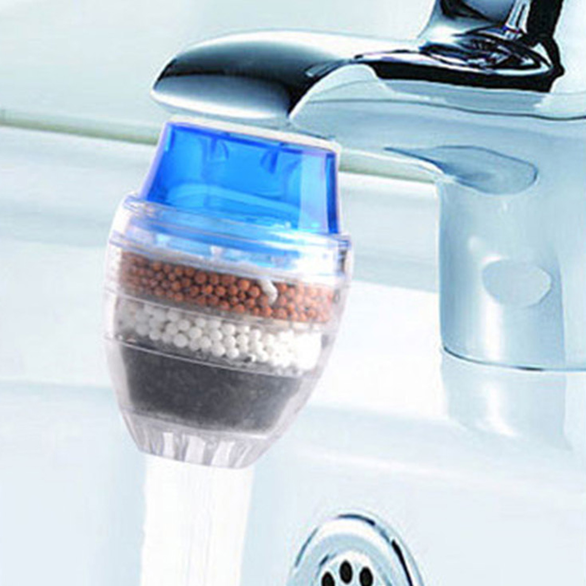 Ein durchsichtiger Wasserfilteraufsatz mit blauer Kappe, gefüllt mit Kugeln in verschiedenen Farben, sitzt auf einem Wasserhahn.
