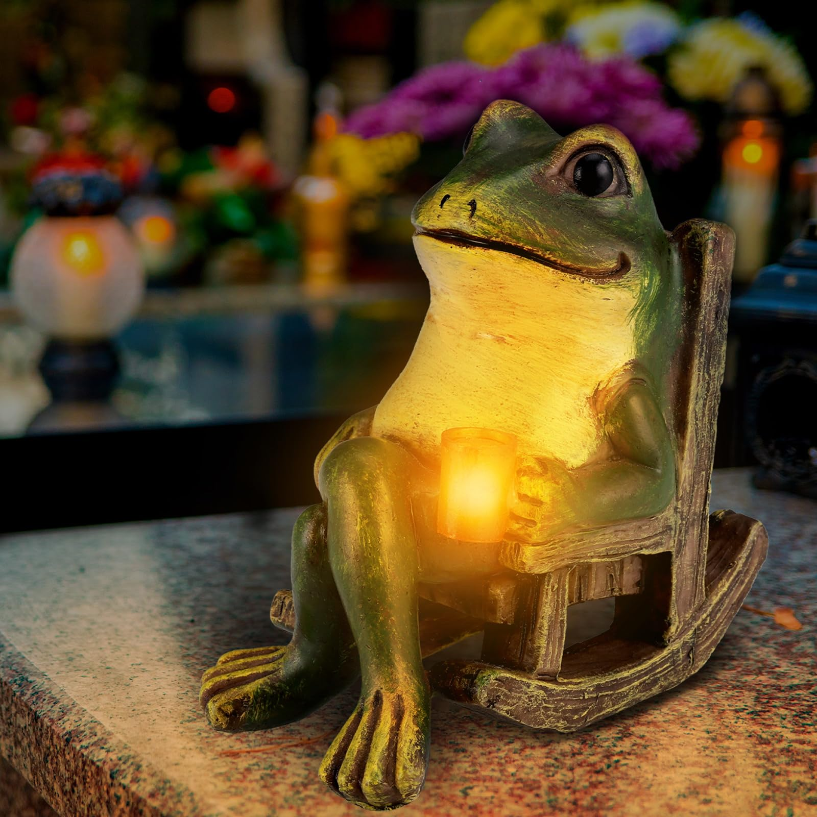 Grüne Froschstatue sitzt in Schaukelstuhl und hält leuchtende Laterne. Blumen im Hintergrund.