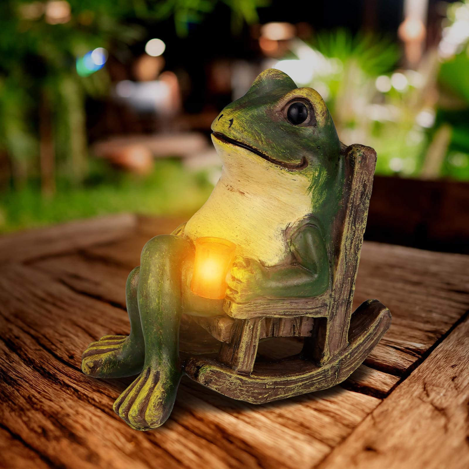 Grüne Froschstatue sitzt in einem Schaukelstuhl und hält eine leuchtende Laterne.