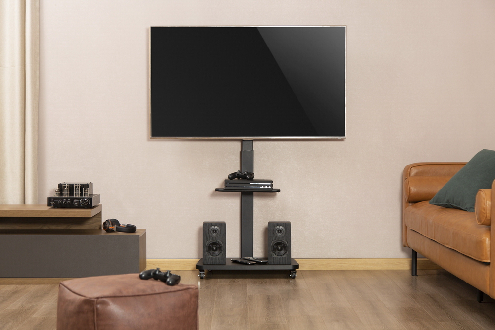 Una grande TV su un supporto con altoparlanti, console e un divano in pelle marrone.