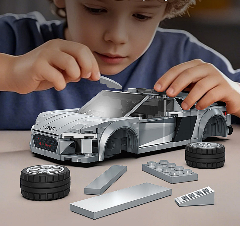 Ein Kind baut einen grauen Audi-Lego-Wagen, daneben liegen lose Teile und Räder.