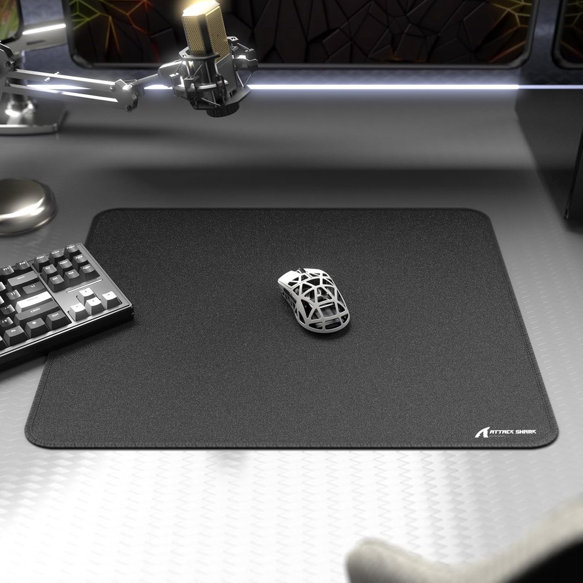 A black mousepad with a white mouse and black keyboard on a desk.