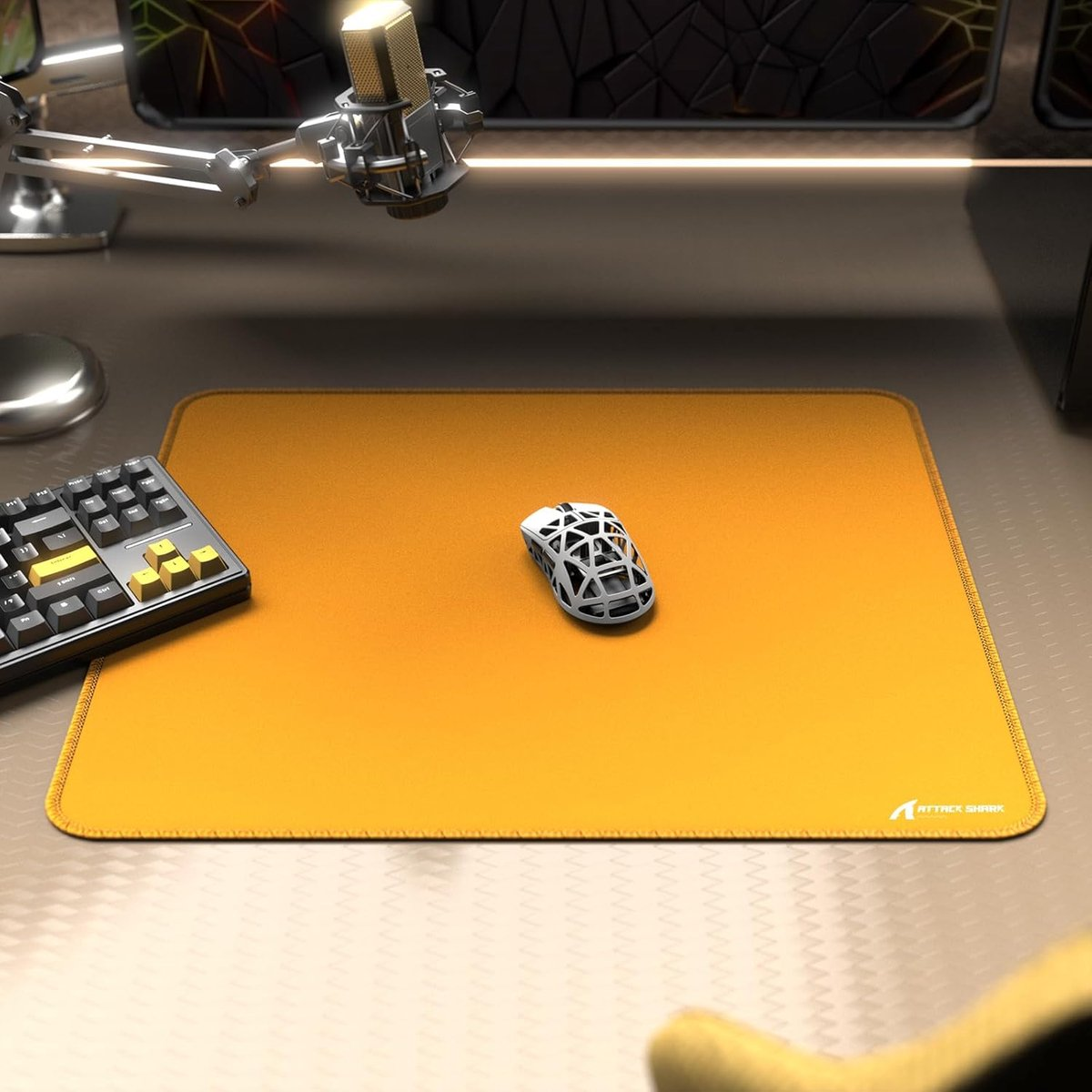 A white gaming mouse on an orange mousepad with a keyboard and microphone.