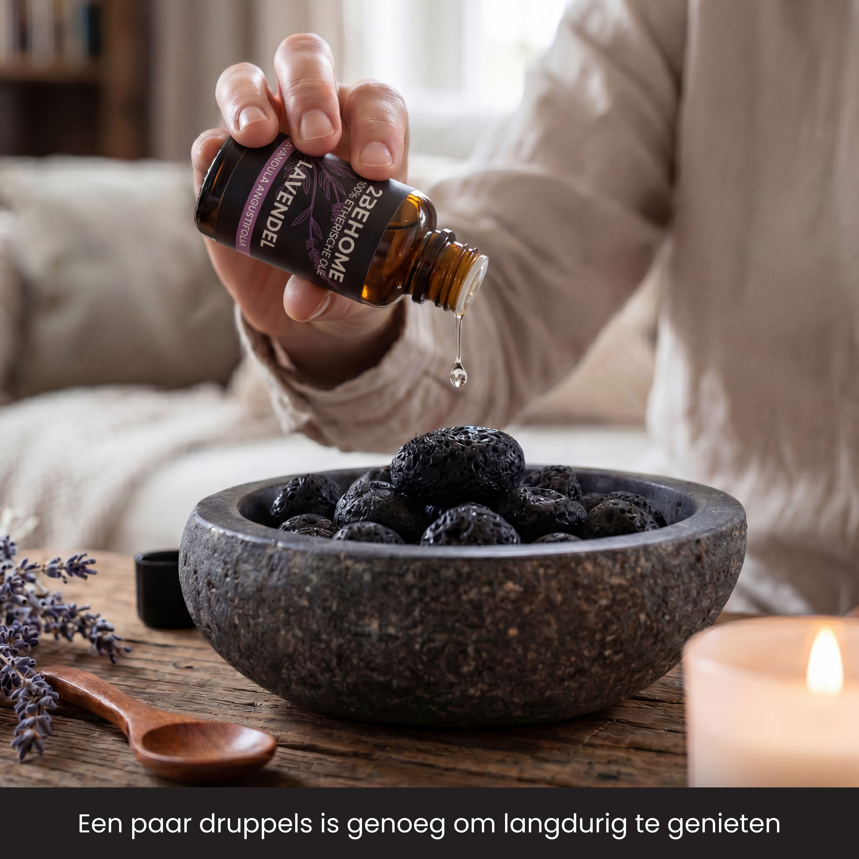 A hand drips lavender oil into a bowl of dark stones.