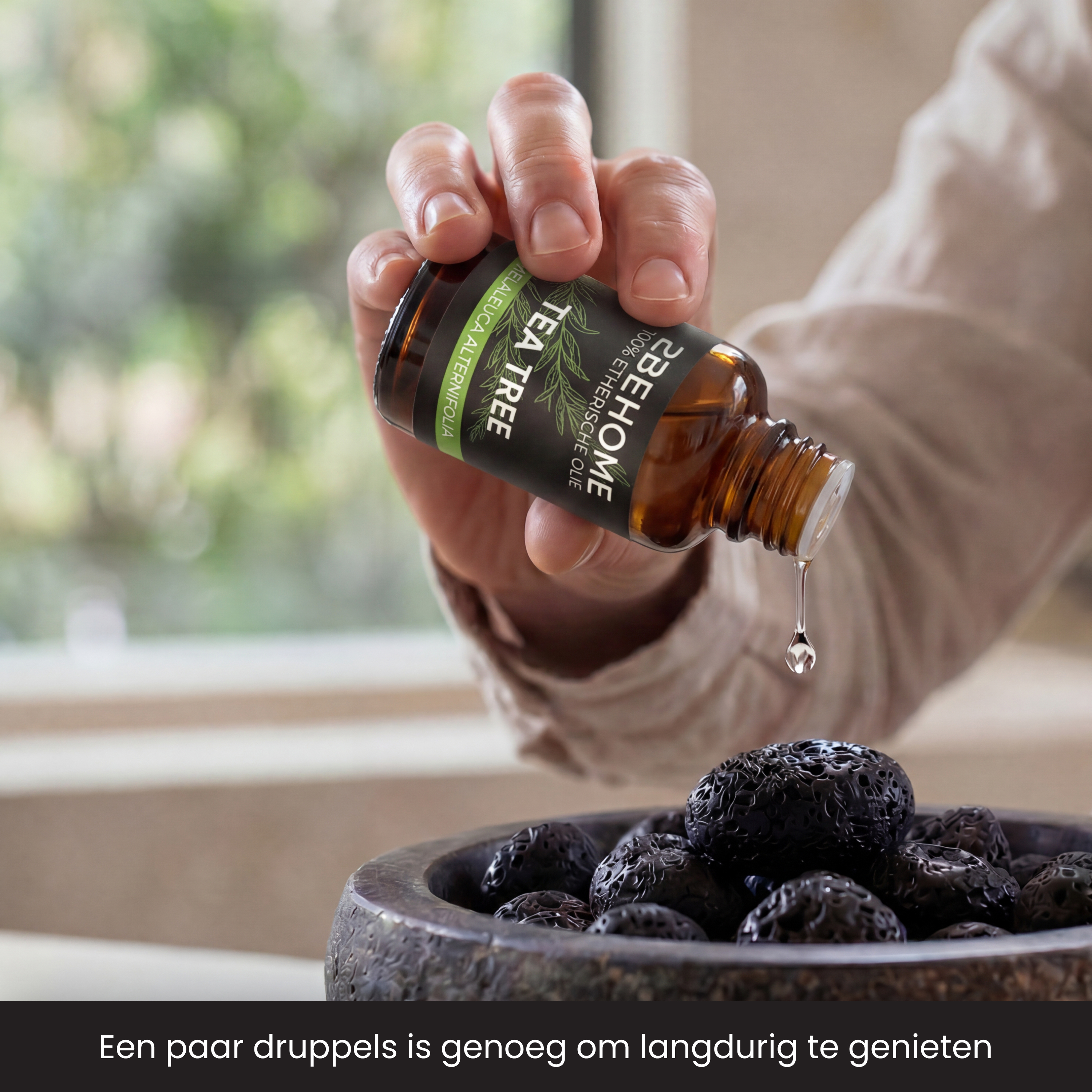 A hand drips tea tree oil from a bottle onto black objects.
