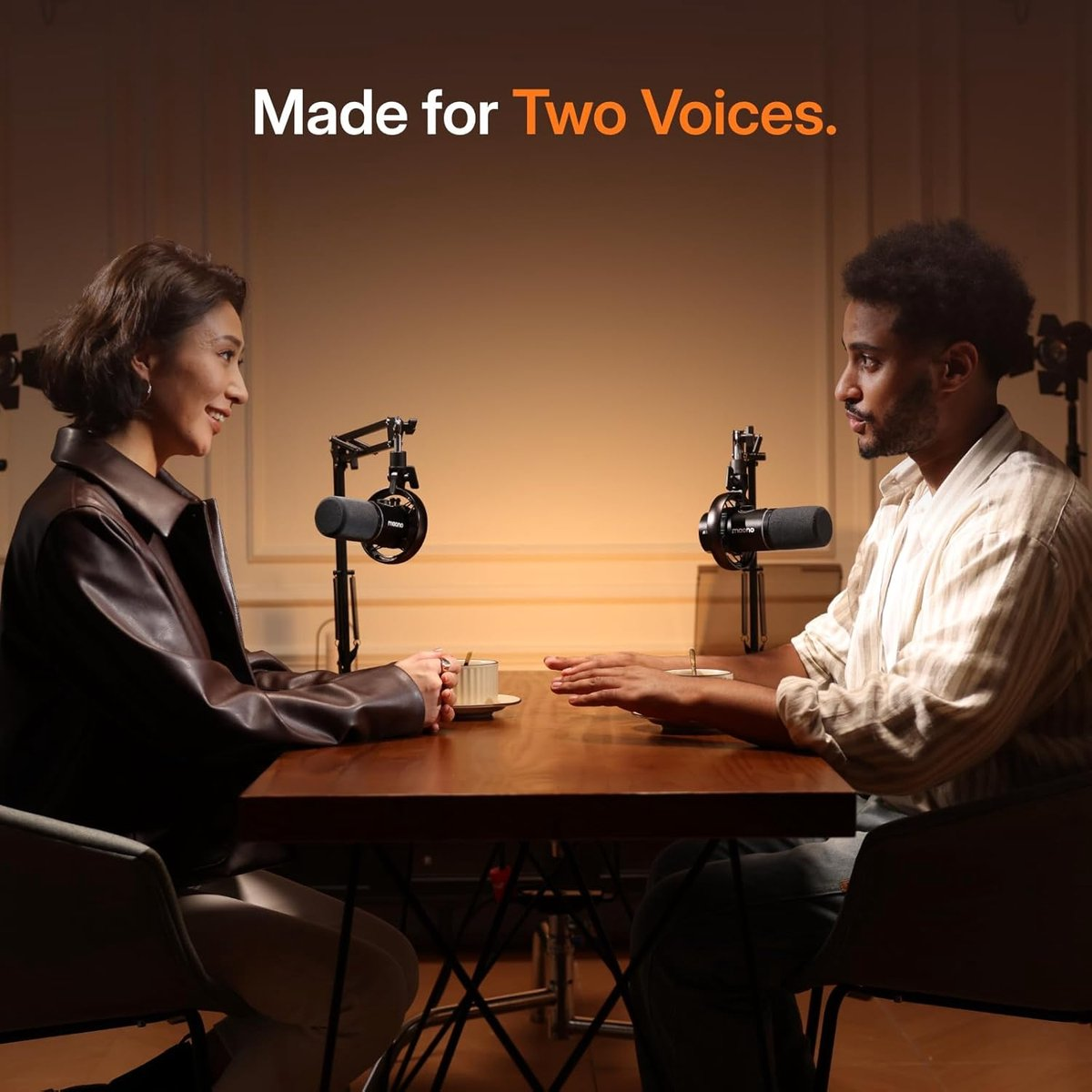 Two people sit at a table with microphones. Text: Made for Two Voices.