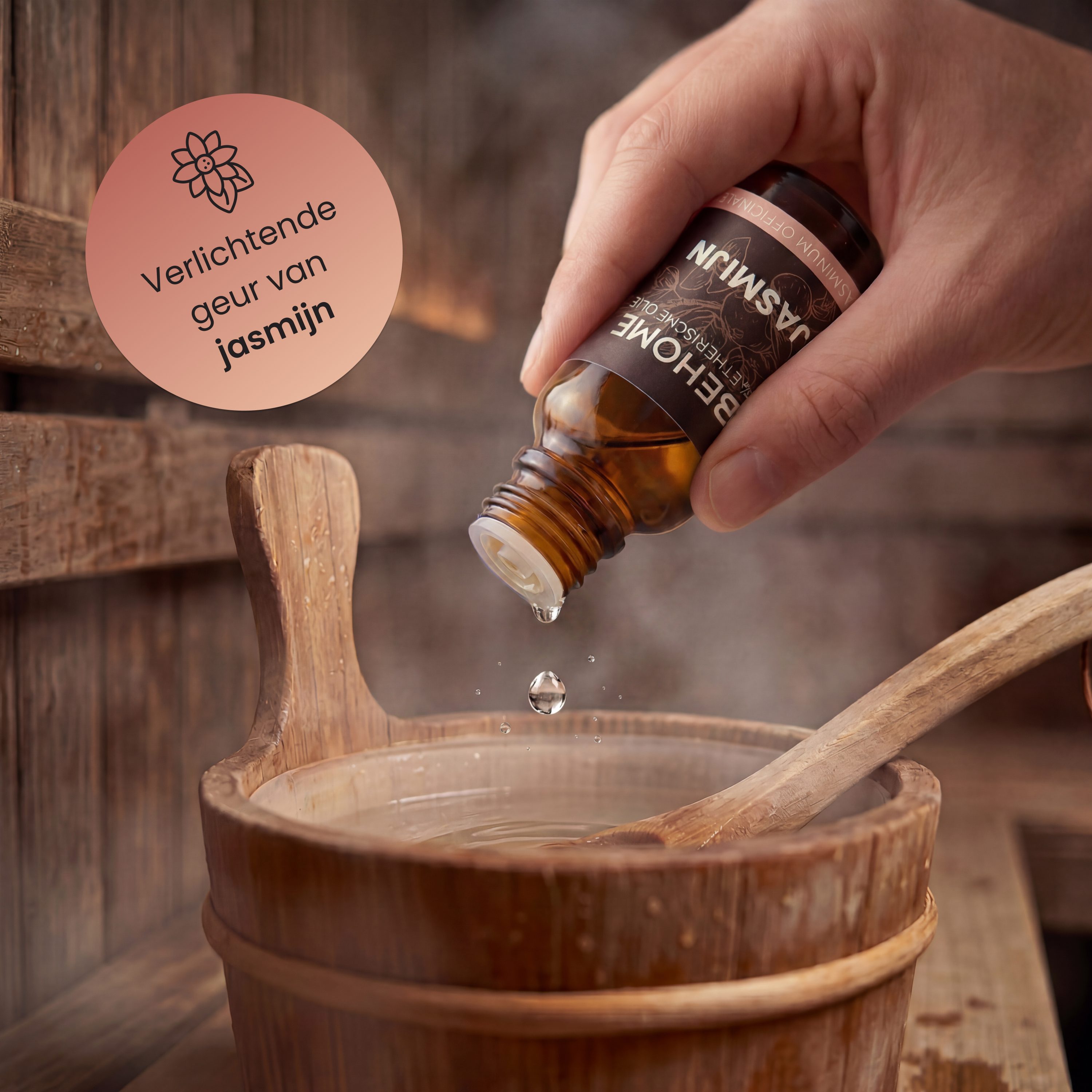 A hand drips jasmine oil into a wooden bucket of water. Steam rises.