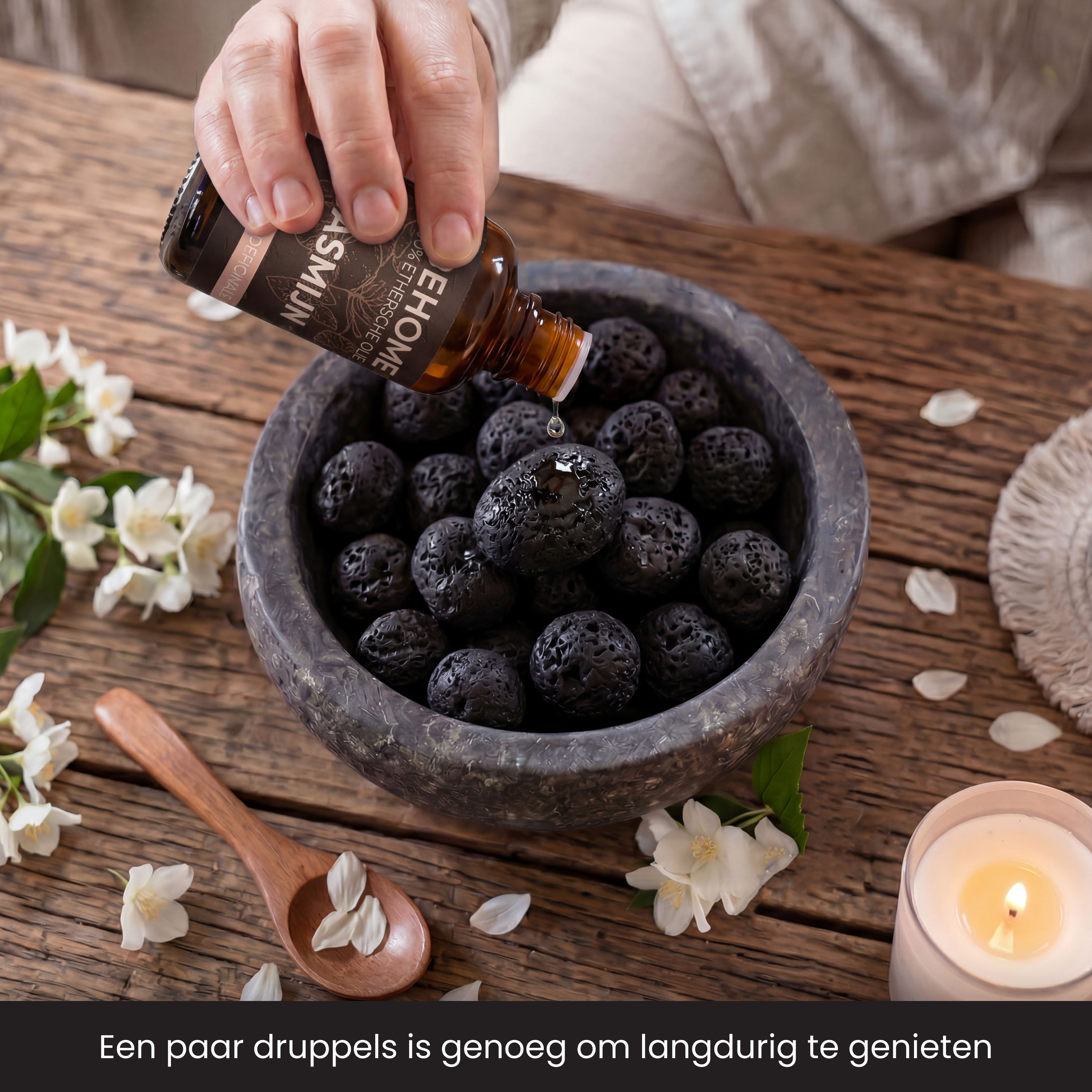 Droplets of essential oil are being dripped onto black lava stones in a bowl.