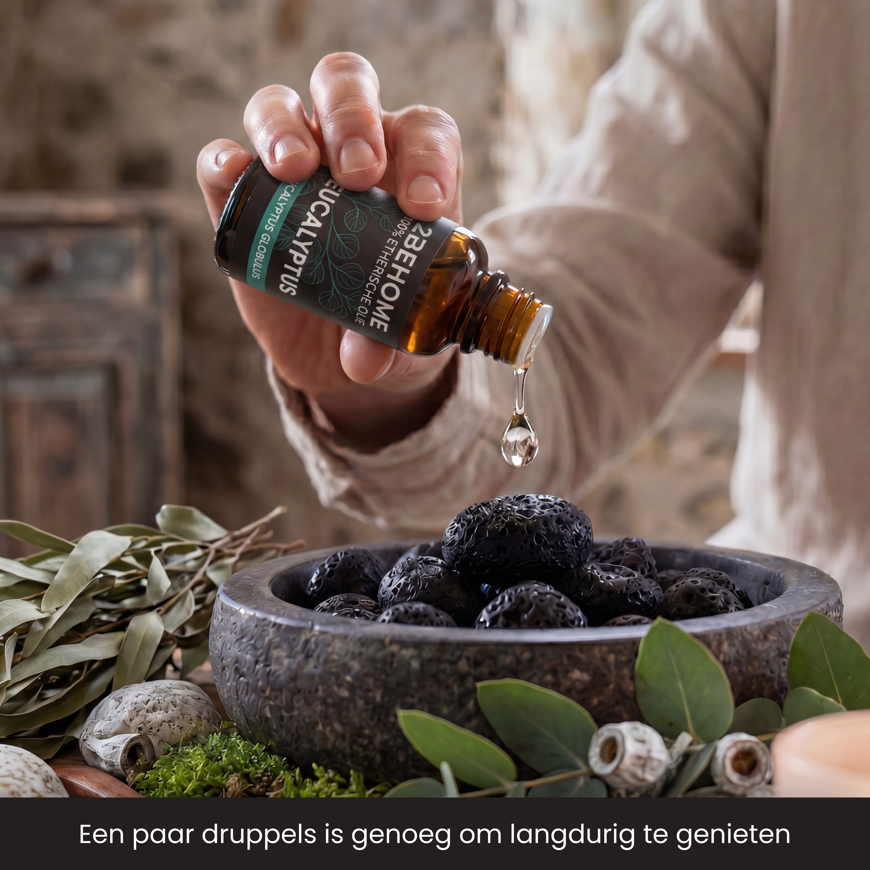 Hand drips oil from bottle onto black balls in bowl with eucalyptus.