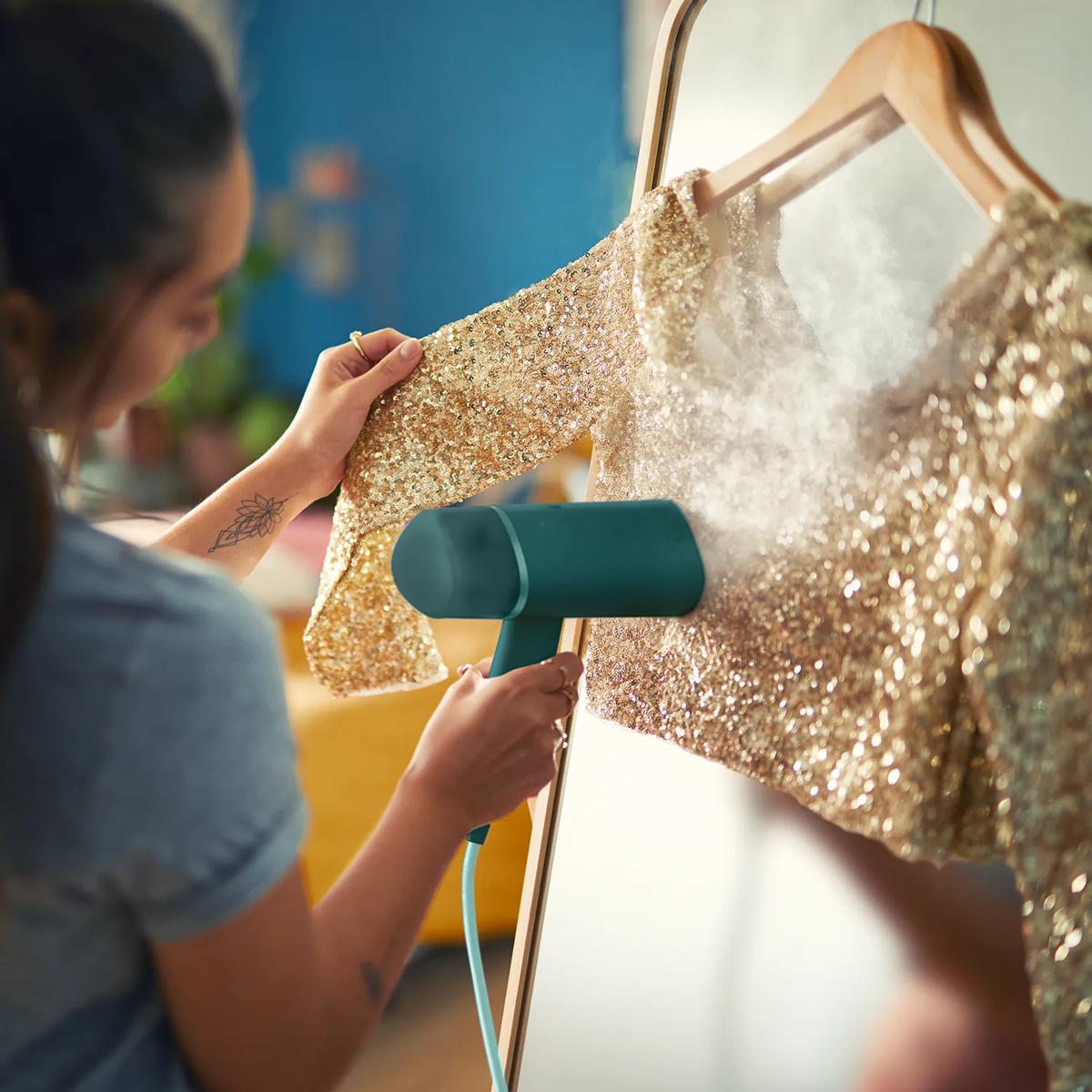 Eine Person glättet ein goldenes Paillettenoberteil mit einem Handdampfer.