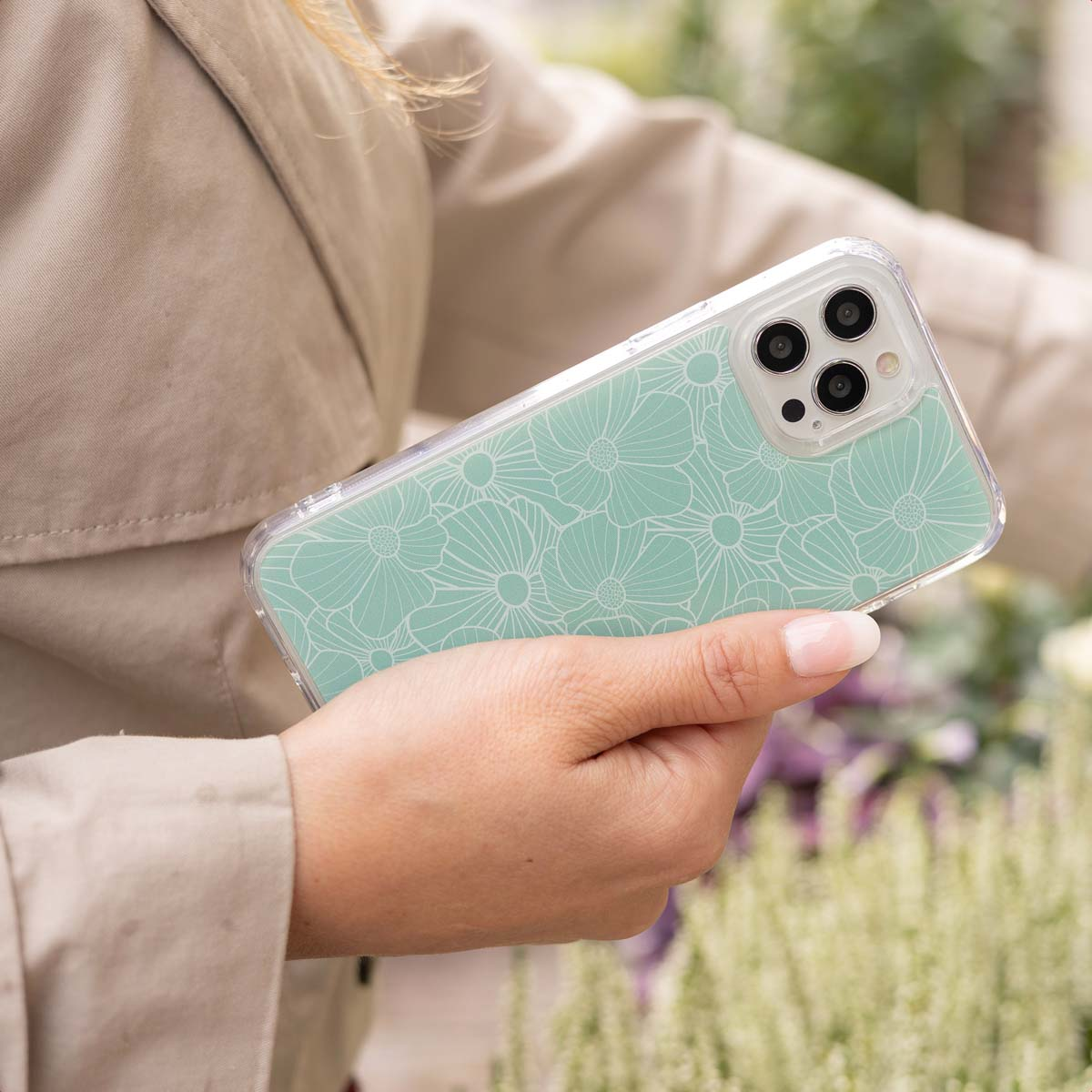 Una mano sujeta un teléfono con un estampado floral turquesa. Plantas al fondo.