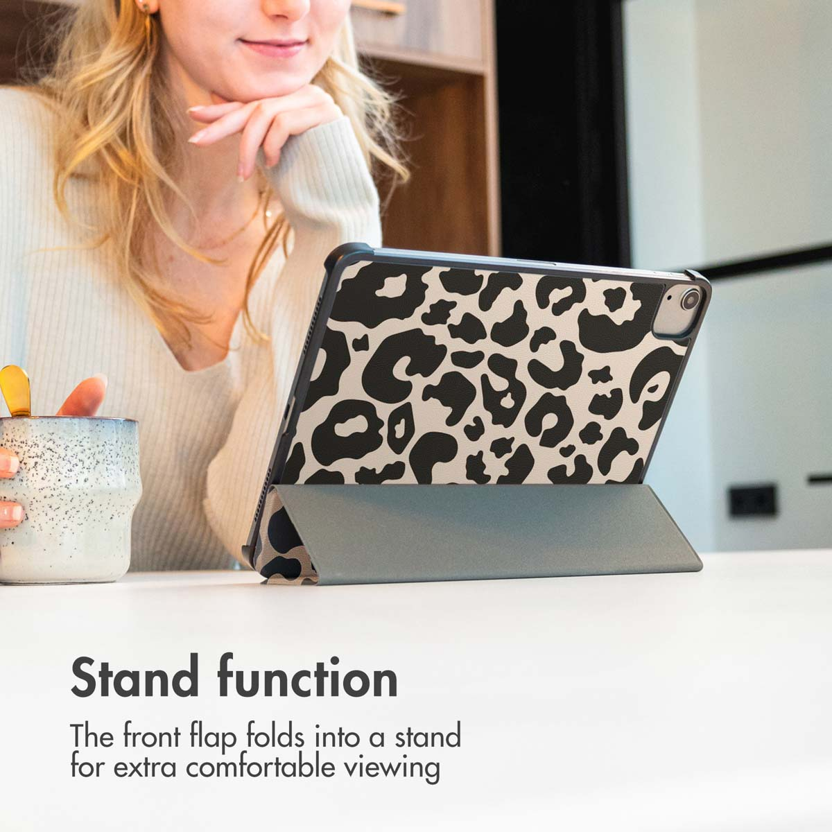 Woman with coffee uses tablet with leopard print case and stand function.