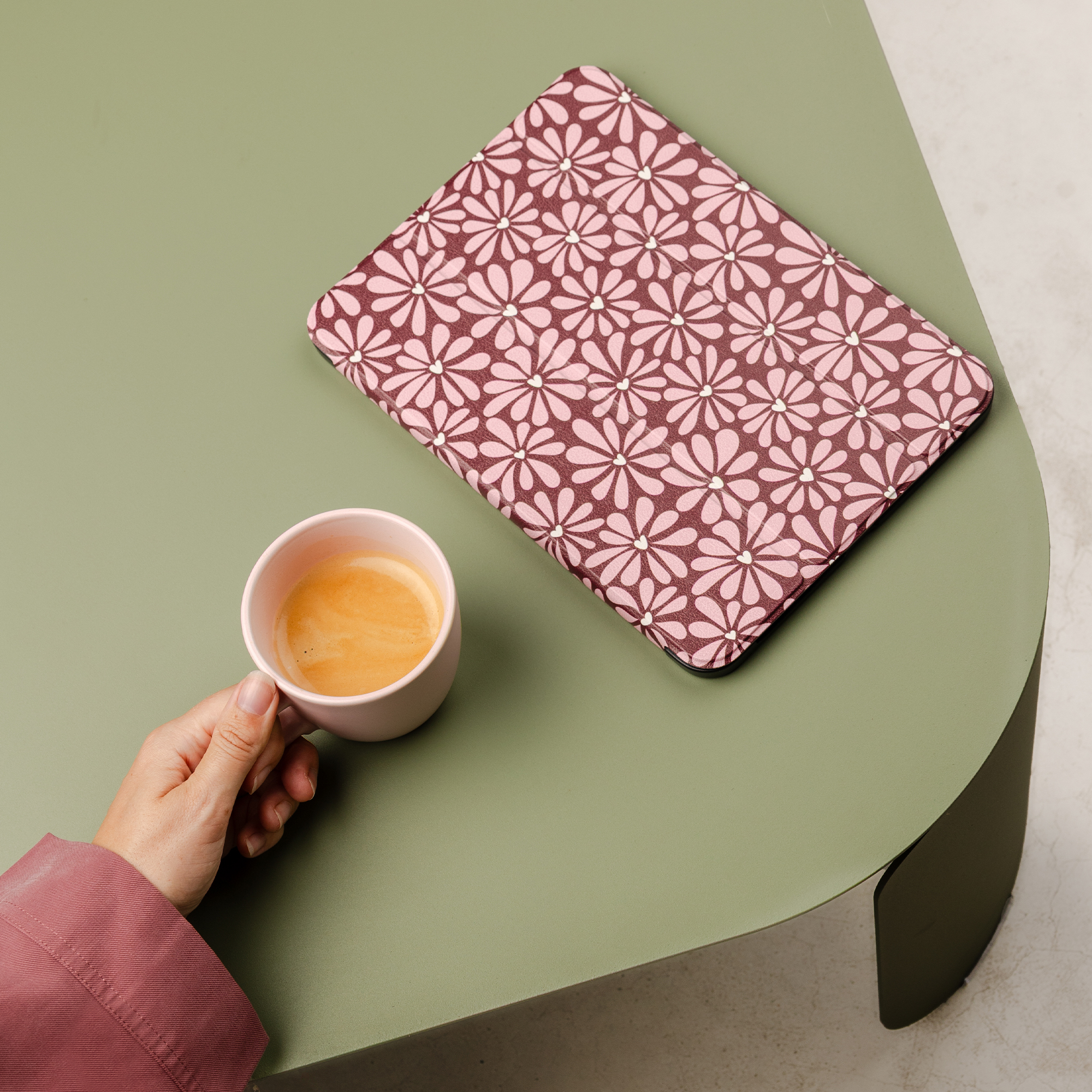 A hand holds a pink cup of coffee next to a floral patterned tray.