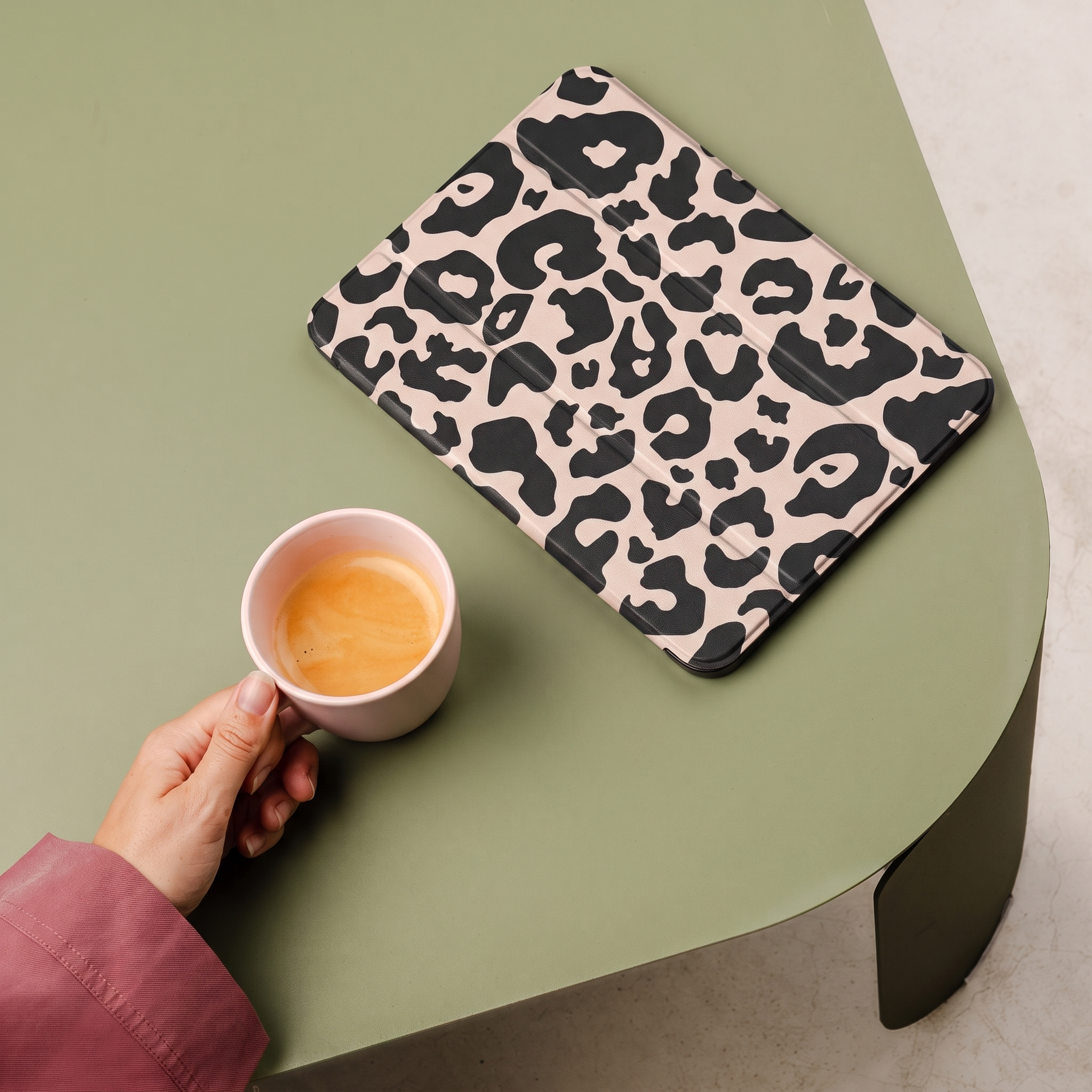 A hand holds a cup of espresso next to a leopard print tablet.