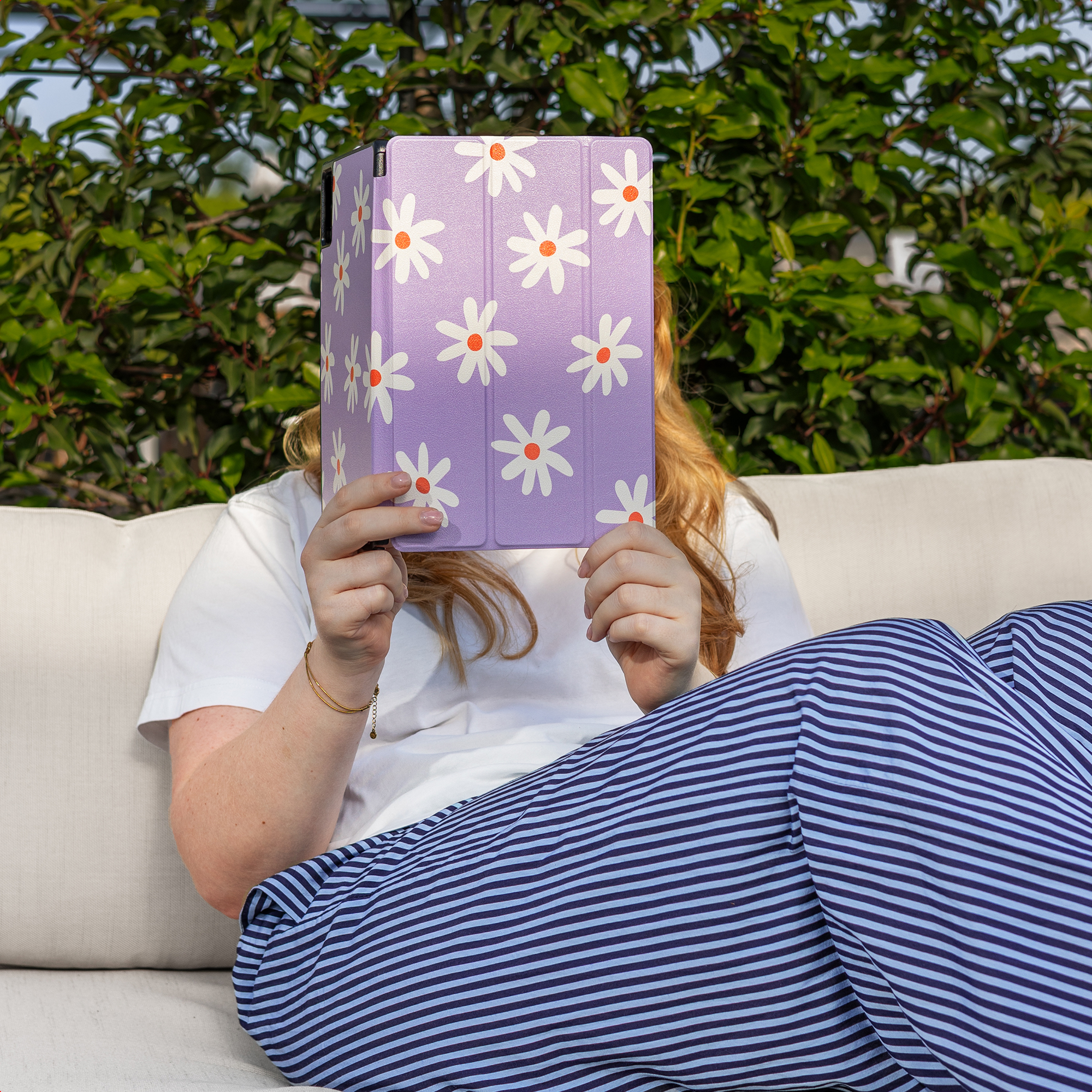 A person sits on a couch holding a purple tablet with a floral pattern.