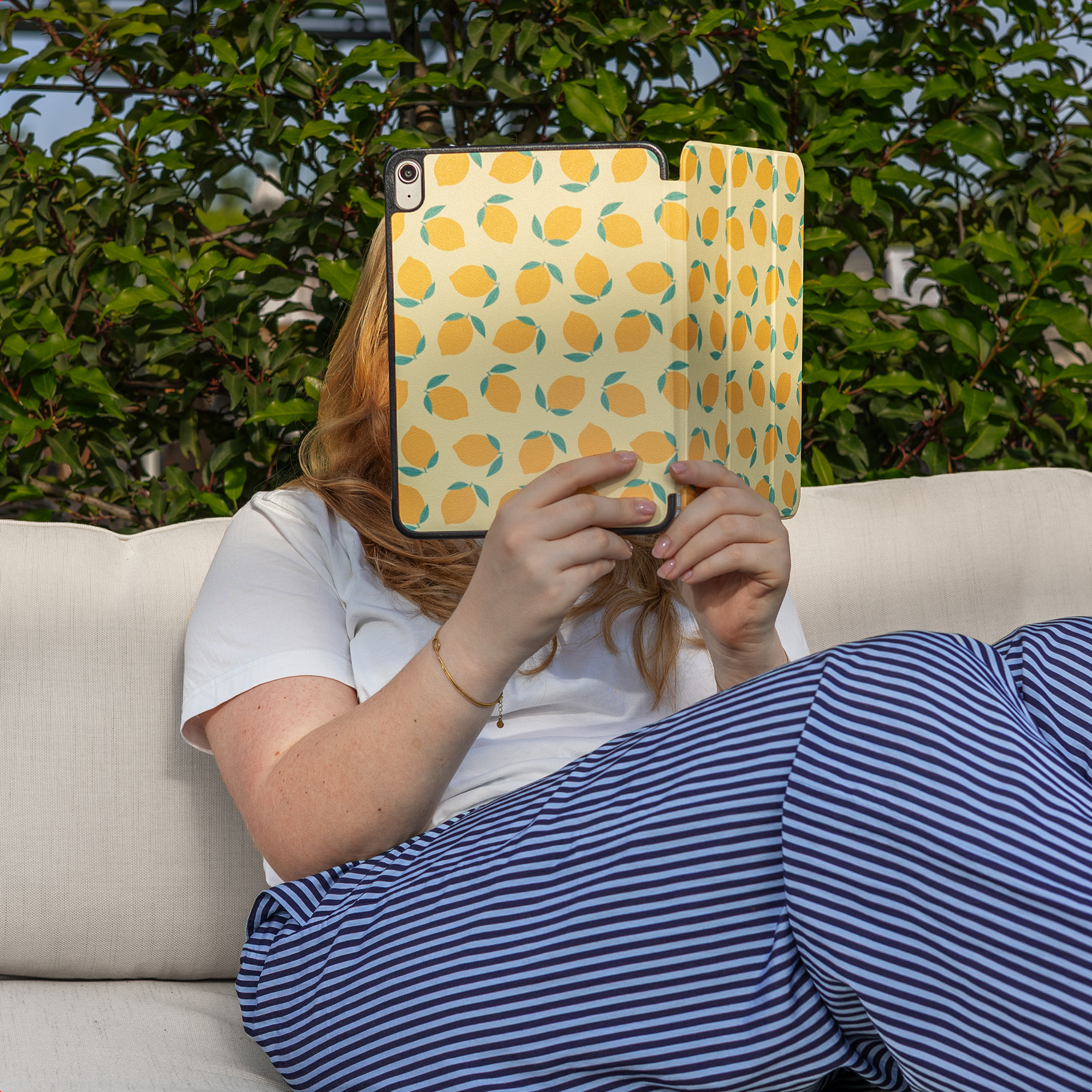 A woman sits outdoors on a sofa holding a lemon-patterned tablet.