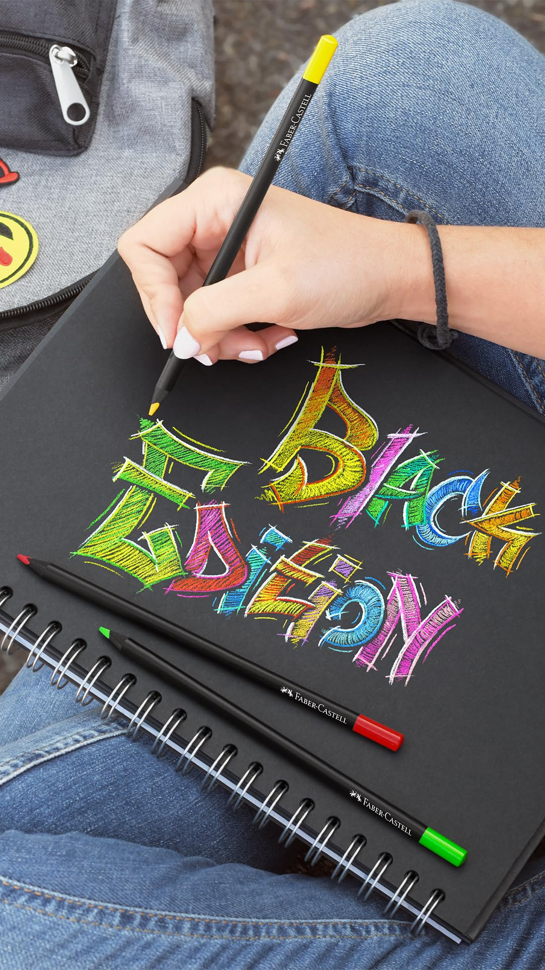 Eine Hand zeichnet mit einem gelben Stift bunte Graffiti auf ein schwarzes Notizbuch.